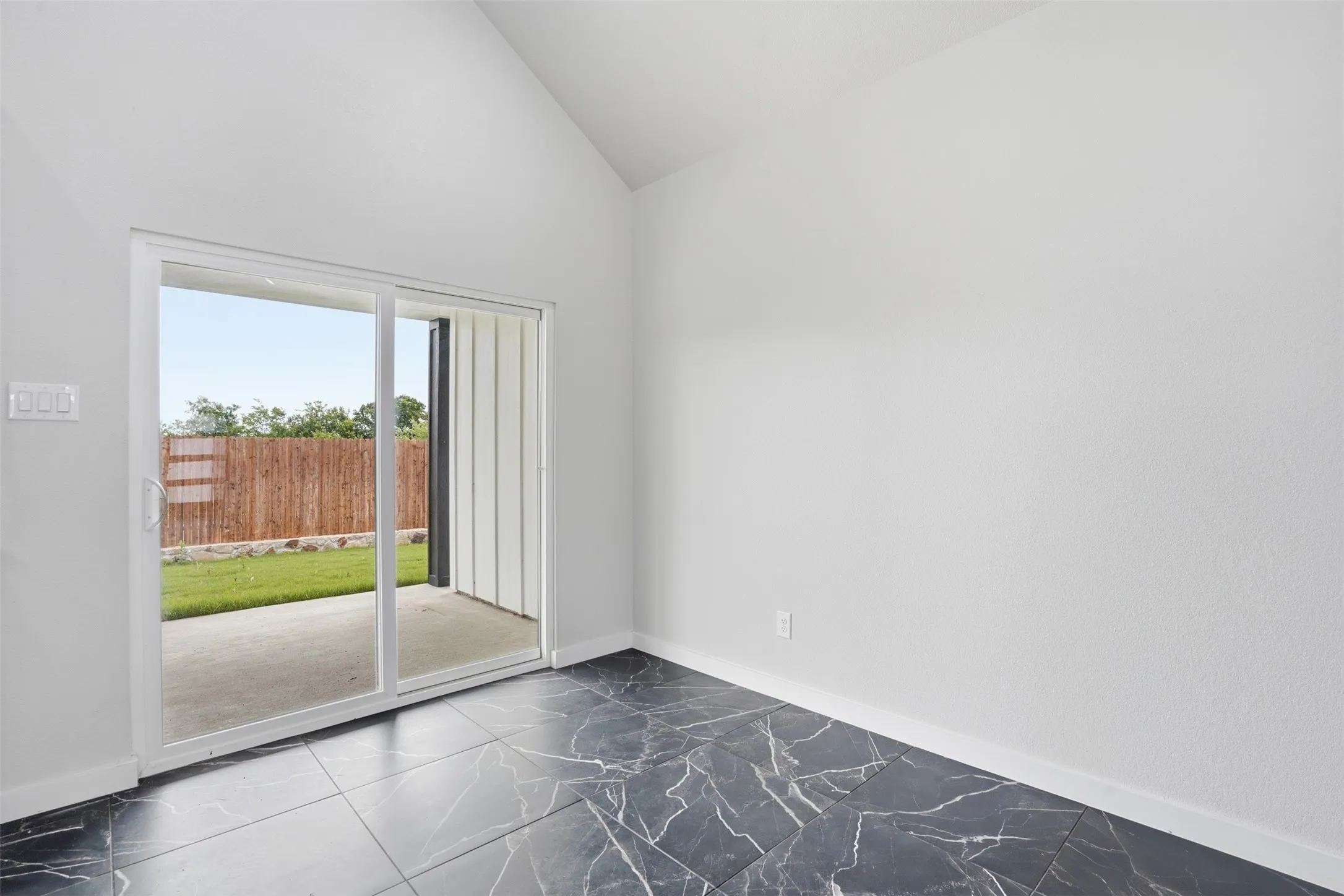 Vaulted ceiling interior space featuring black marble-look tile flooring and white baseboards