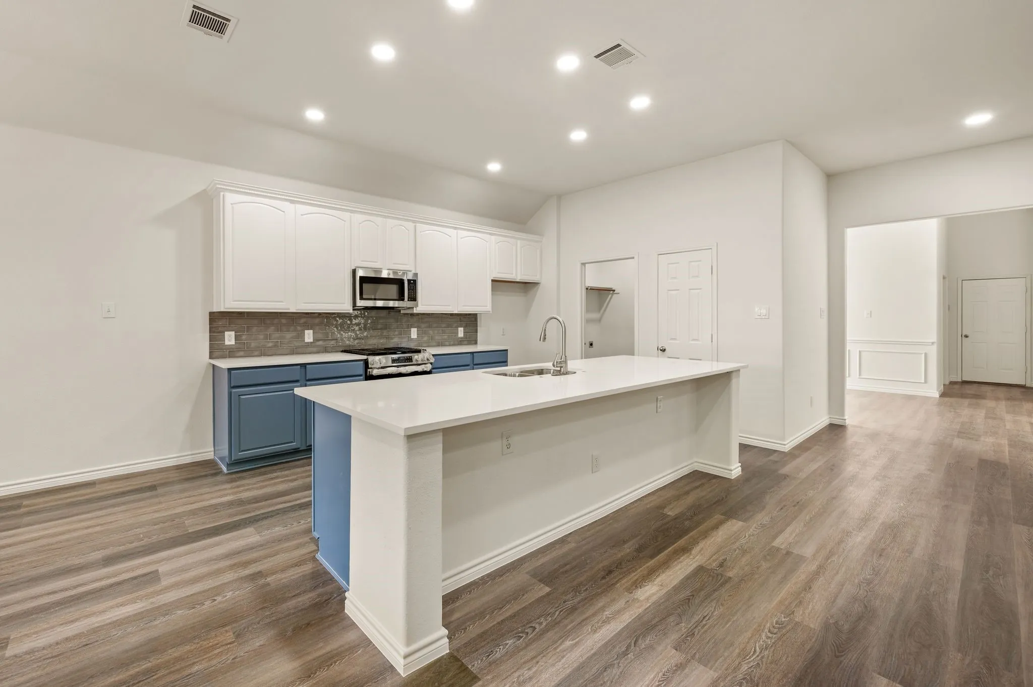 Modern kitchen featuring white cabinetry, a large center island with quartz countertop, stainless steel appliances, tile backsplash, recessed ceiling lighting, and wood-finish flooring throughout the open-concept living area