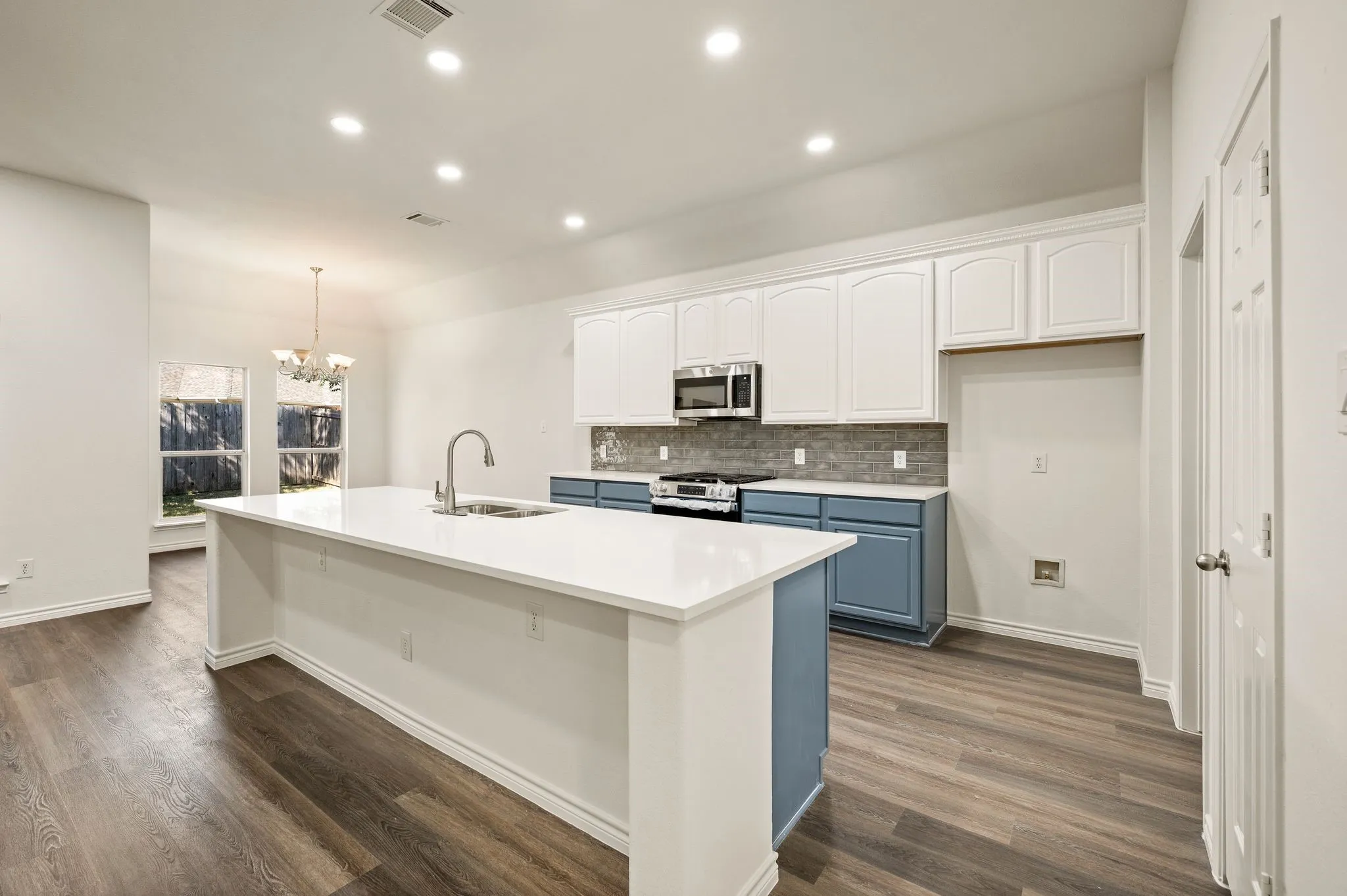 Open-concept kitchen featuring an expansive island with a built-in sink, white cabinetry, a tiled backsplash, and wood-finish flooring