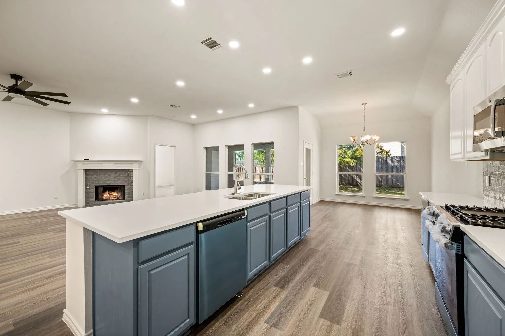 Open-concept kitchen and living area featuring a large center island with white quartz countertop, blue cabinetry with multiple storage options, and stainless steel gas range