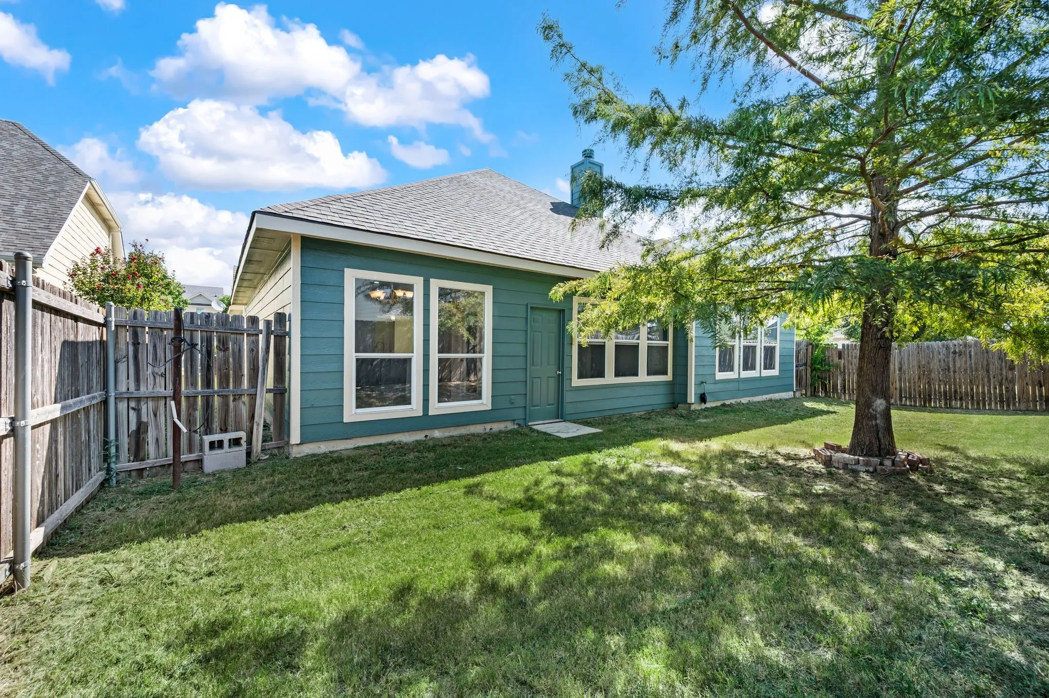 Charming single-story home with board-and-batten exterior in soft blue-green, featuring multiple large windows and a covered entry