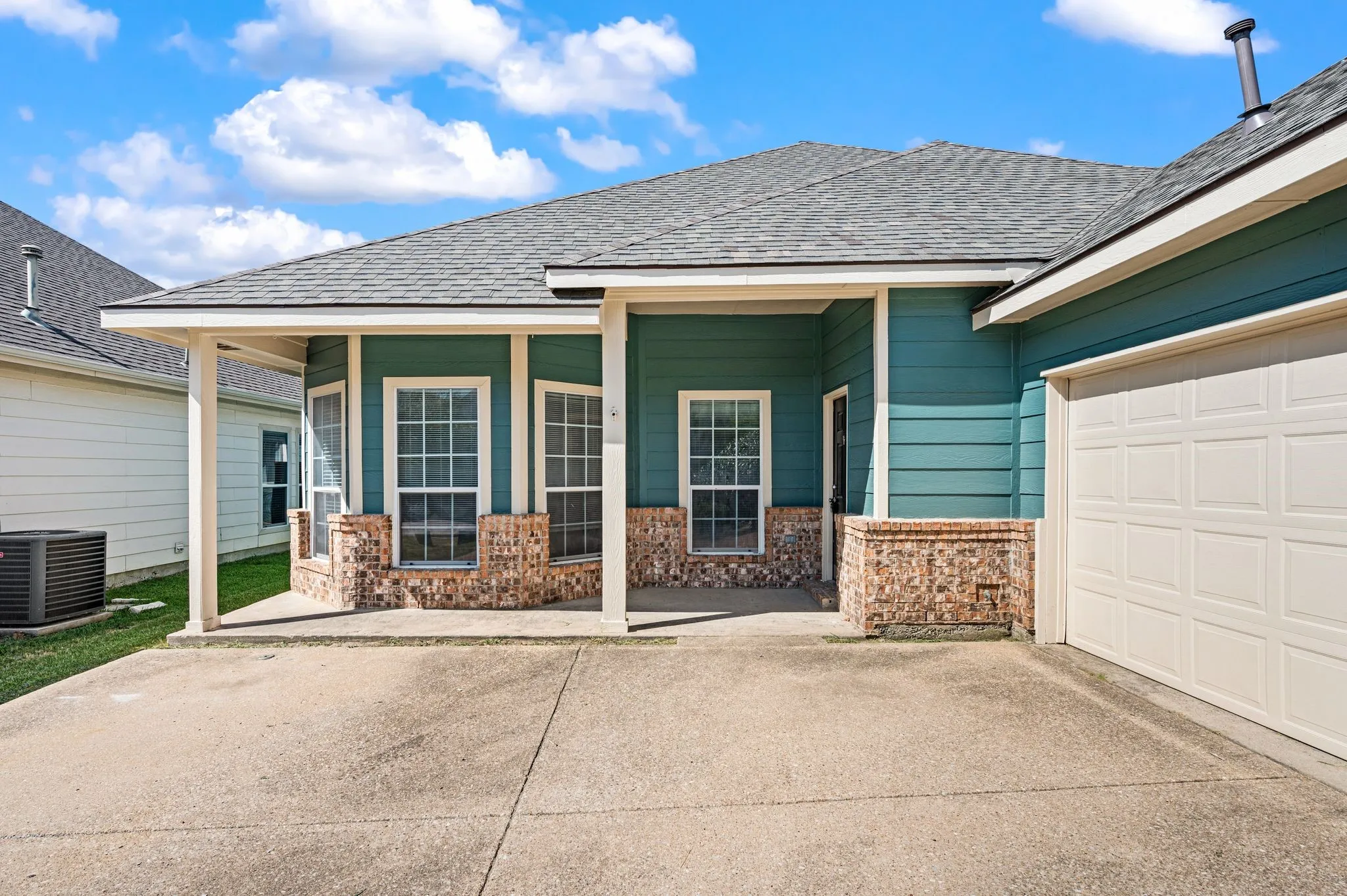 Covered front porch with French doors and stone veneer detailing, complemented by a spacious driveway and attached two-car garage