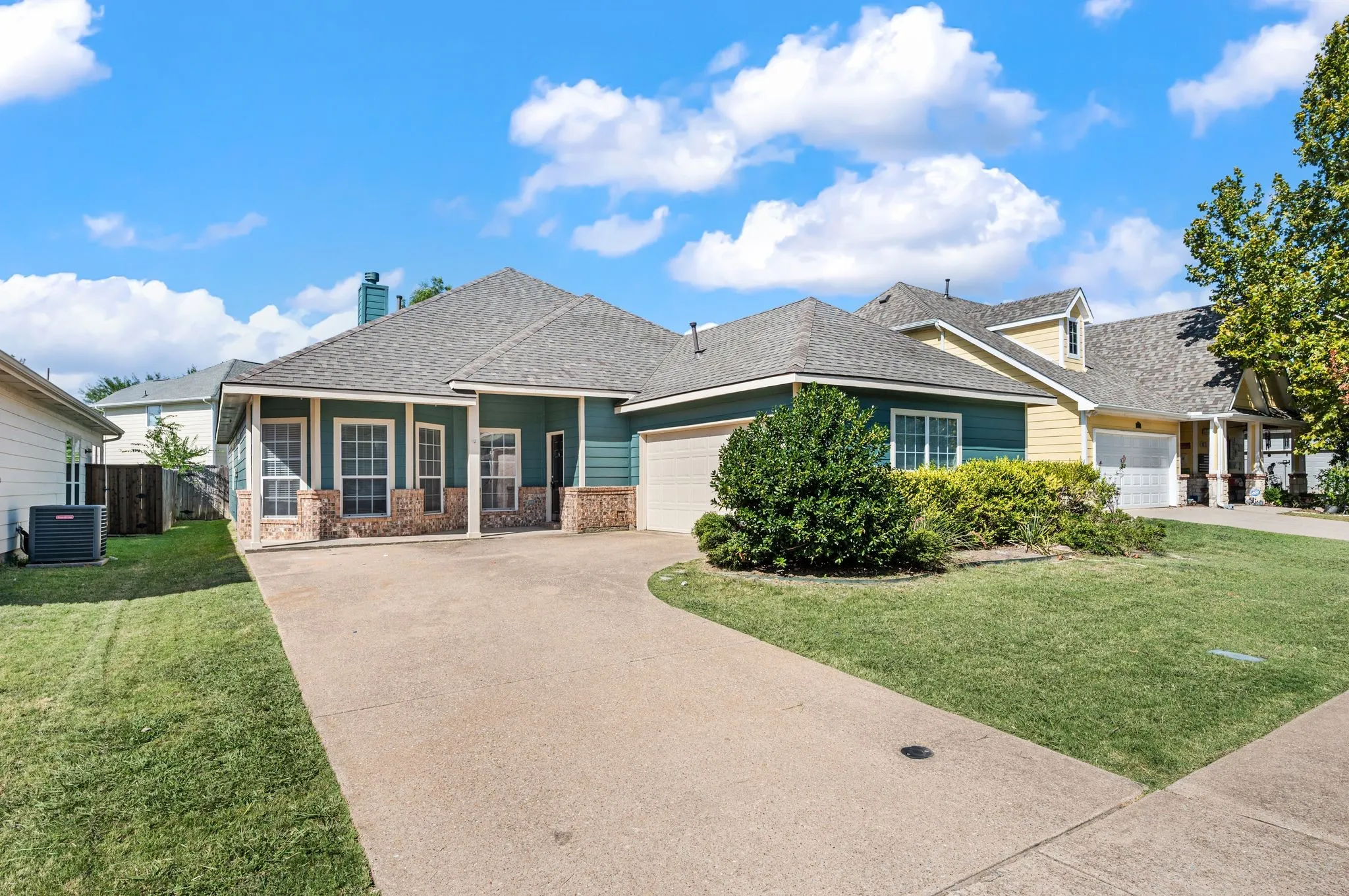 Concrete driveway with a curved entrance, mature landscaping, and a two-car garage