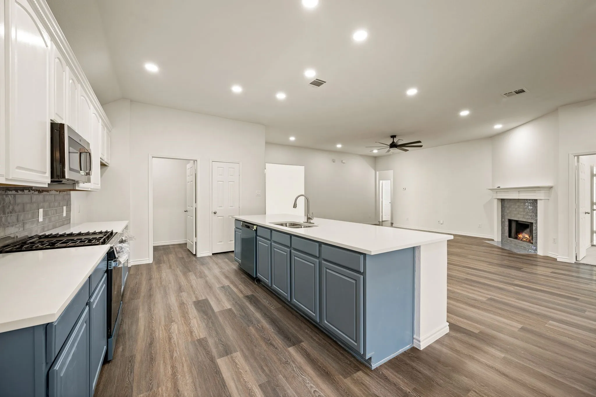 Open-concept kitchen and living area featuring a large island with white quartz countertop, blue cabinetry with brushed nickel hardware, stainless steel appliances, wood-finish flooring throughout, recessed lighting, and a ceiling fan