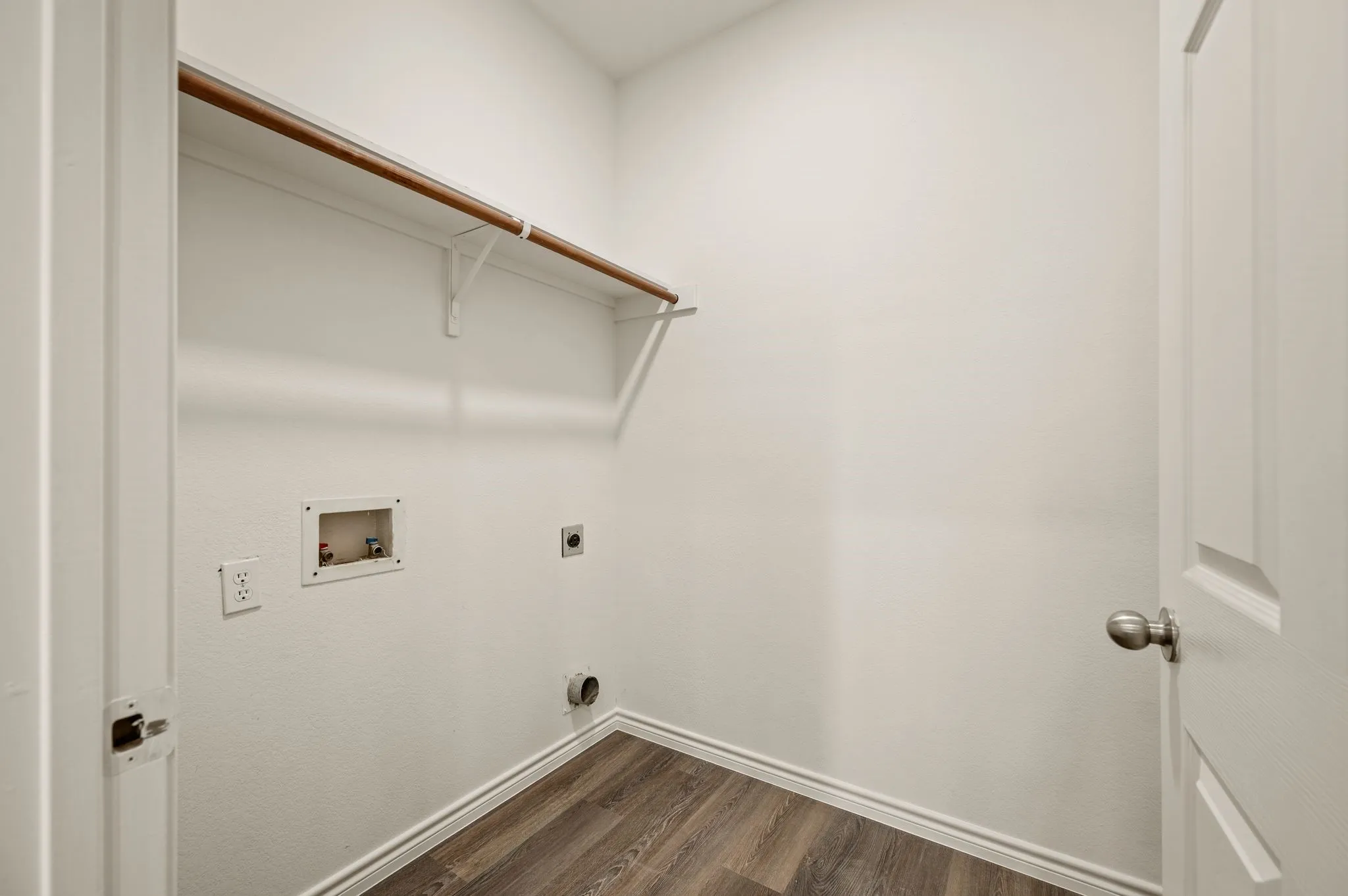 Dedicated laundry room featuring wood-finish flooring, white drywall construction, a rod-style hanging system, and practical built-in shelving