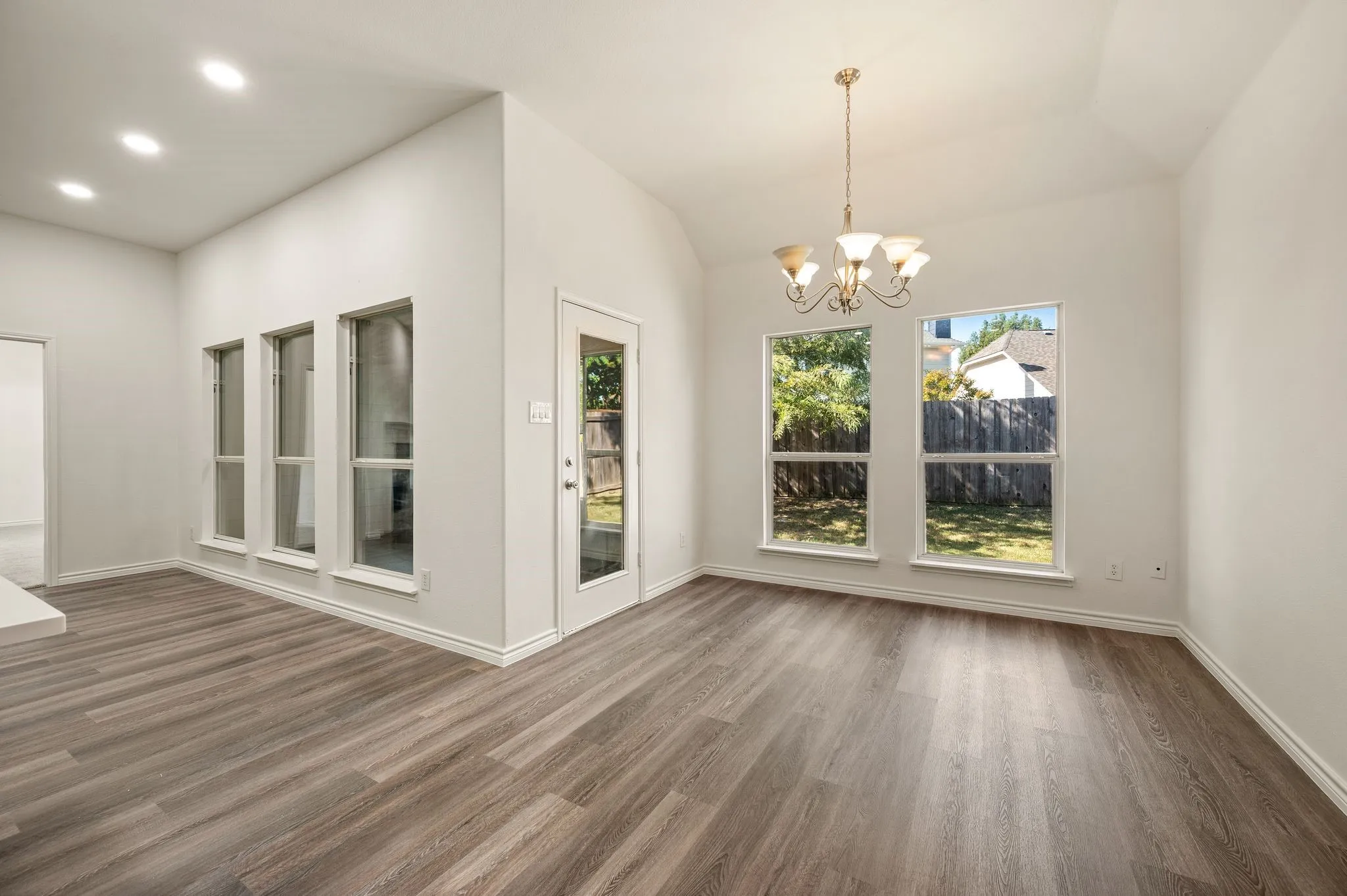 Wood-finish flooring throughout, recessed ceiling lighting, vaulted ceiling, multiple large windows, and a glass-paneled exterior door