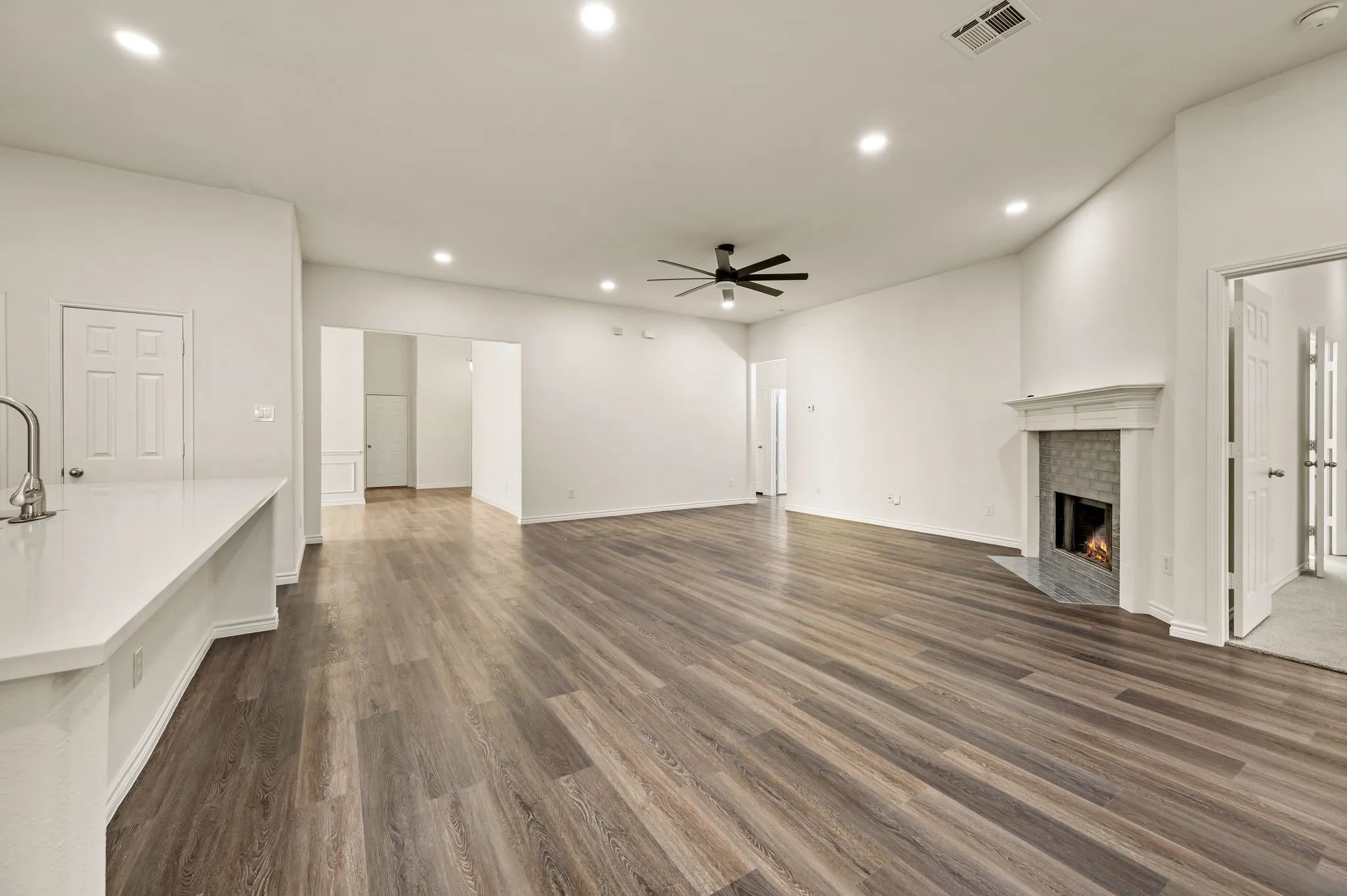 Spacious open-concept living area featuring wood-finish flooring throughout, recessed ceiling lighting, and a ceiling fan
