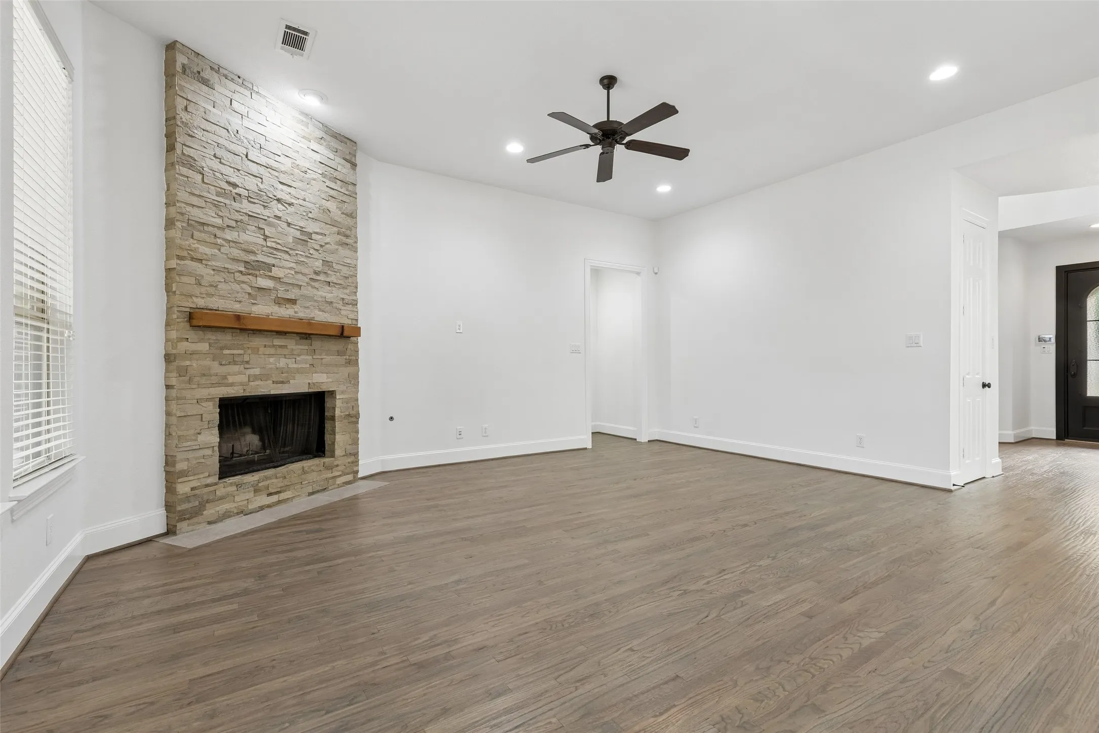 Living room with refinished hardwood floors and floor to ceiling stacked stone gas fireplace.