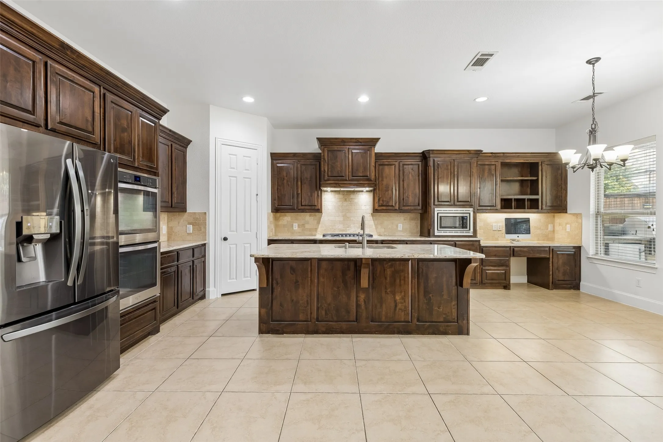Kitchen with granite counter tops, tile backsplash, SS appliances, oversized kitchen island, planning desk, and walk in pantry.