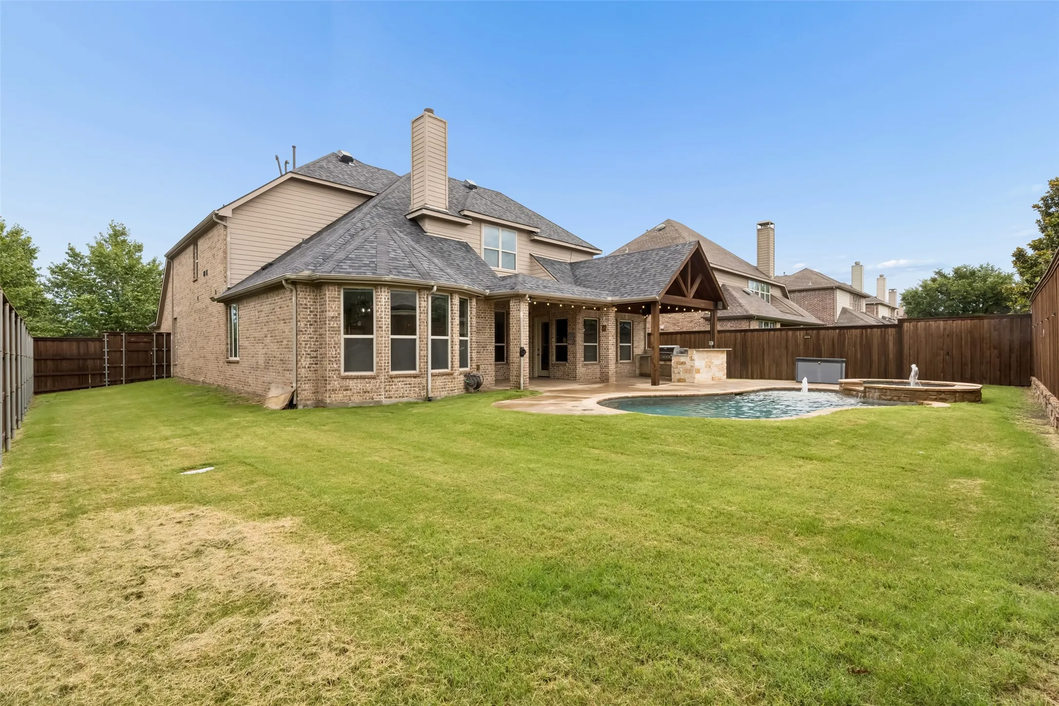 Back yard view of pool & spa, extended covered patio with built in outdoor kitchen, and large grass area.