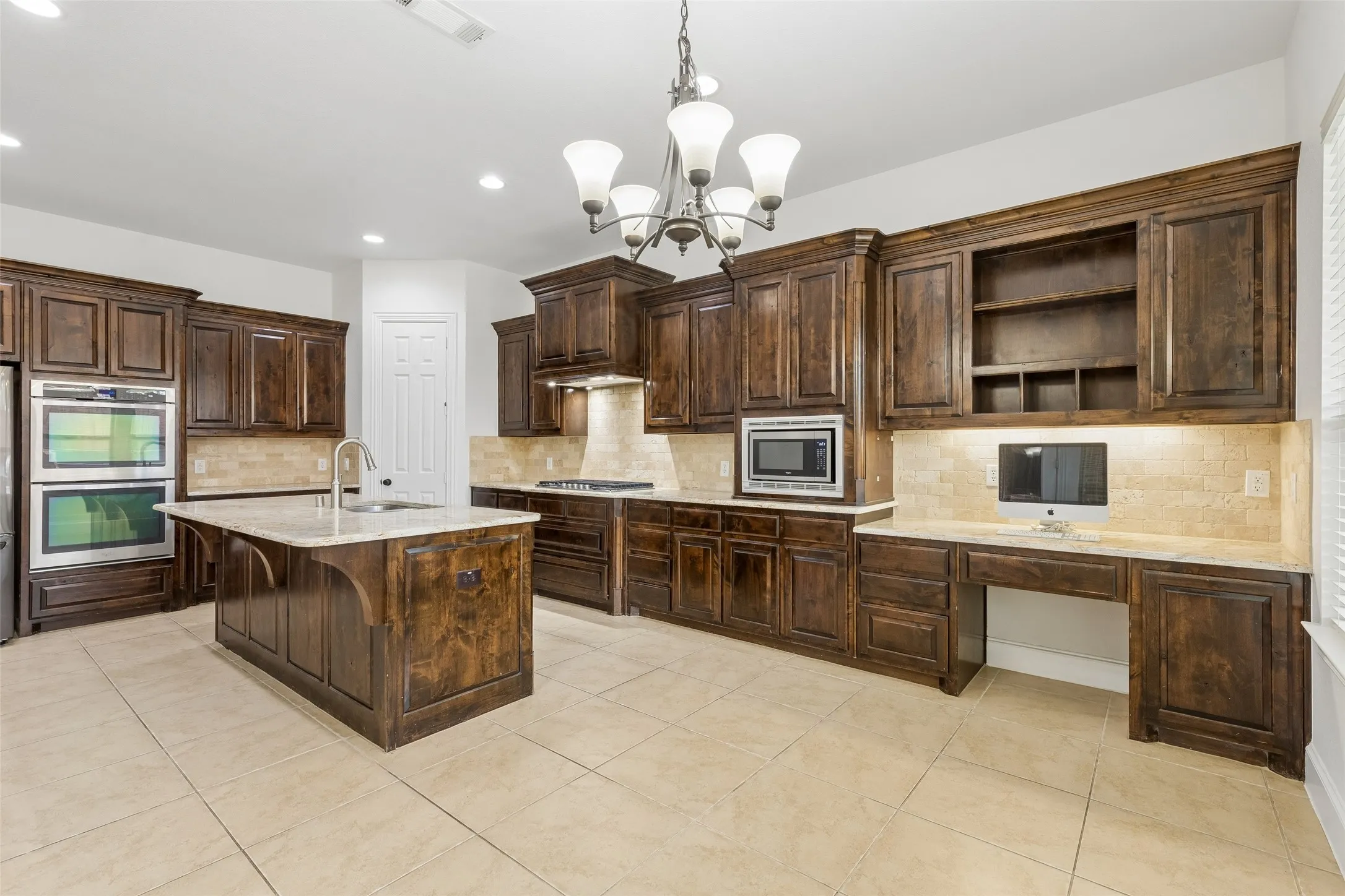 Kitchen with granite counter tops, tile backsplash, SS appliances, oversized kitchen island, planning desk, and walk in pantry.