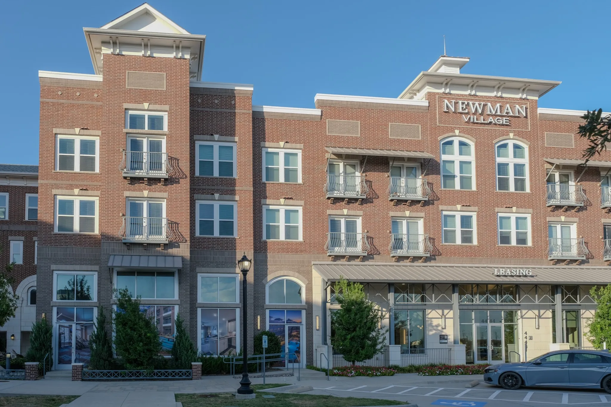 Brick and stone facade building featuring multiple balconies with wrought iron railings, a prominent signage, and a ground-floor leasing office with large storefront windows