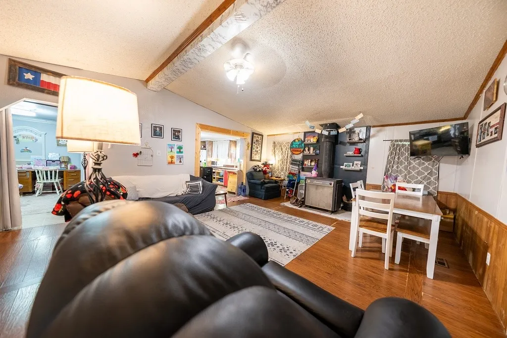Open concept living area featuring wood-finish flooring, white paneling, and a vaulted ceiling