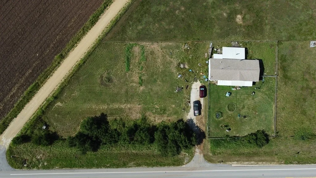 Aerial view of a property featuring a single-story residence with a light-colored roof, a gravel driveway, and a partially fenced yard