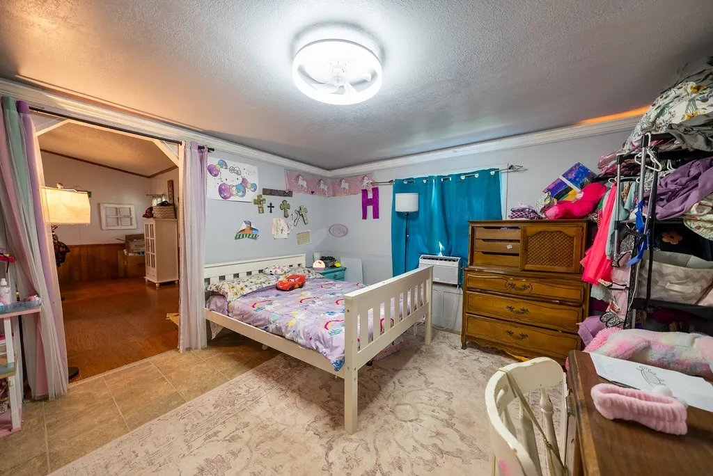 Recessed ceiling light fixture illuminating a room featuring tile flooring, a window with blue curtains, and an open doorway leading to an interior space with wood-finish flooring