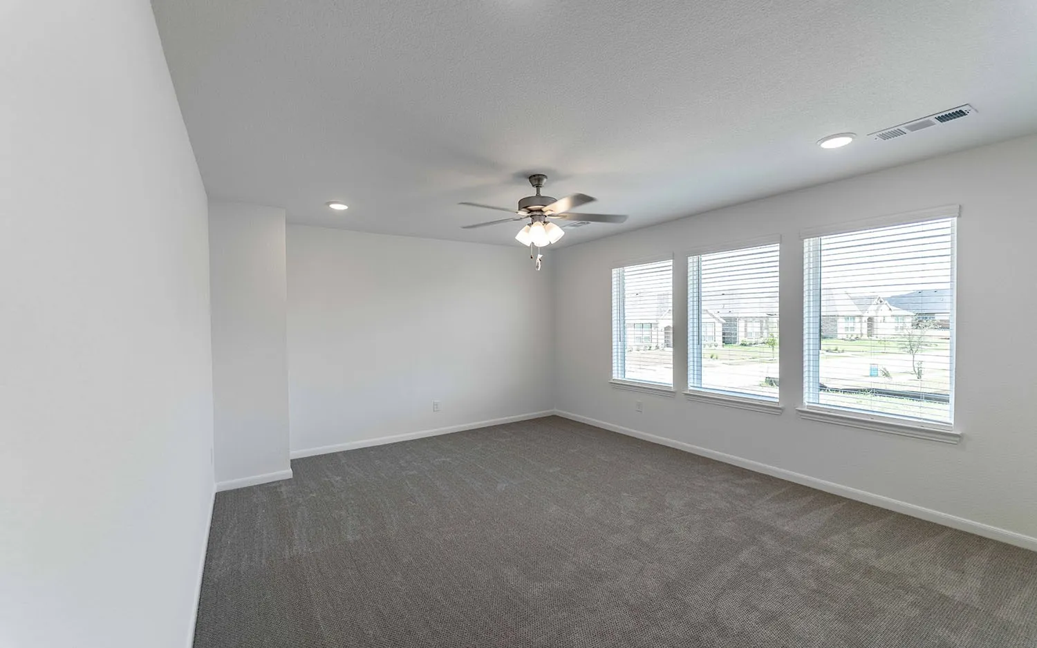Spacious room featuring three large windows, gray carpeting, a ceiling fan with integrated lighting, and recessed lighting