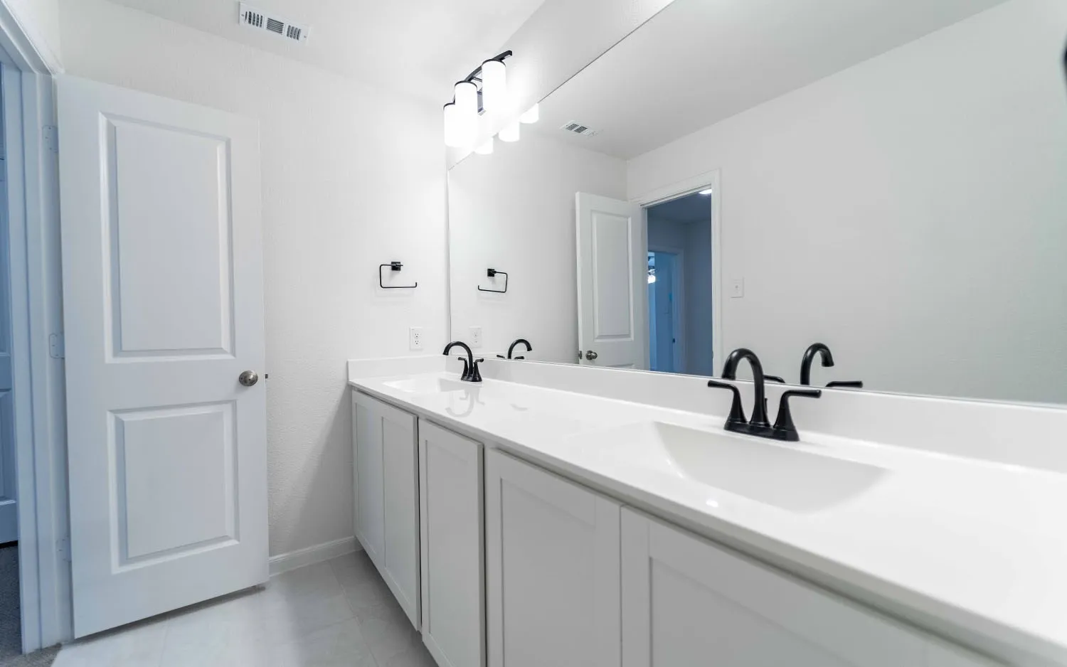 Dual vanity featuring integrated sinks, matte black faucets, white shaker-style cabinetry, and a full-width mirror