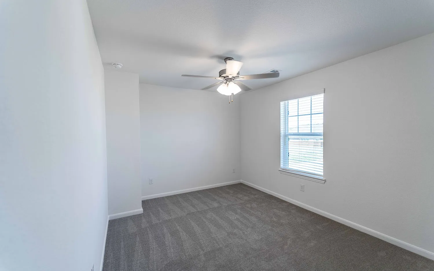 Room featuring light gray patterned carpeting, white walls, a single window with horizontal blinds, and a ceiling fan with integrated lighting