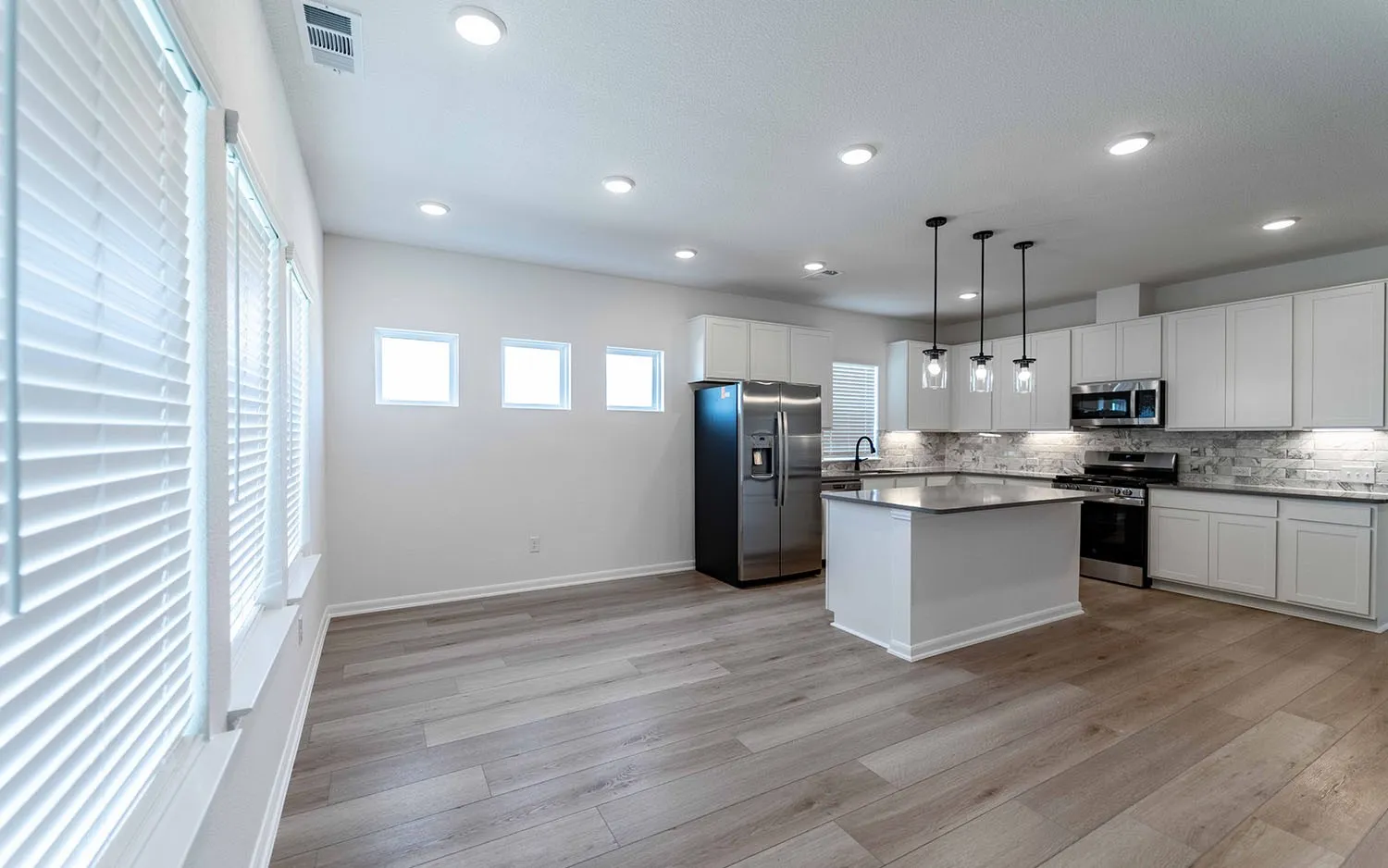 Open-concept living area with wood-finish flooring, recessed lighting, and multiple windows