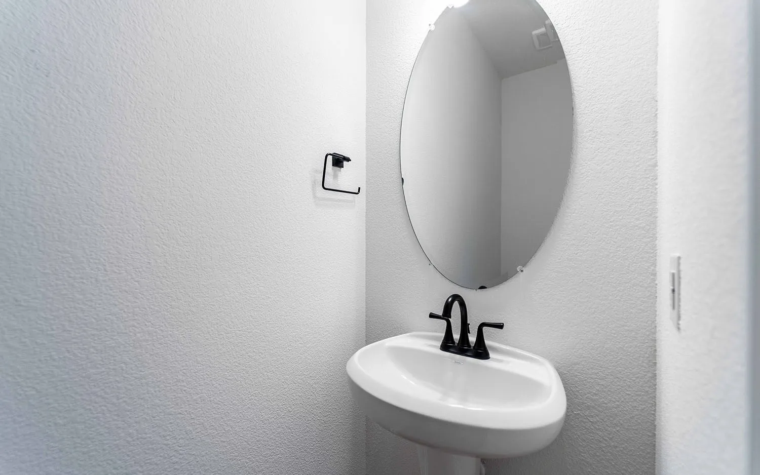 Pedestal sink with a black-finished faucet and an oval wall mirror