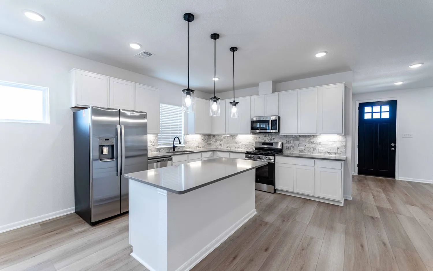 Modern kitchen featuring a central island with a light-toned countertop, white cabinetry, a tiled backsplash, stainless steel appliances, and wood-finish flooring