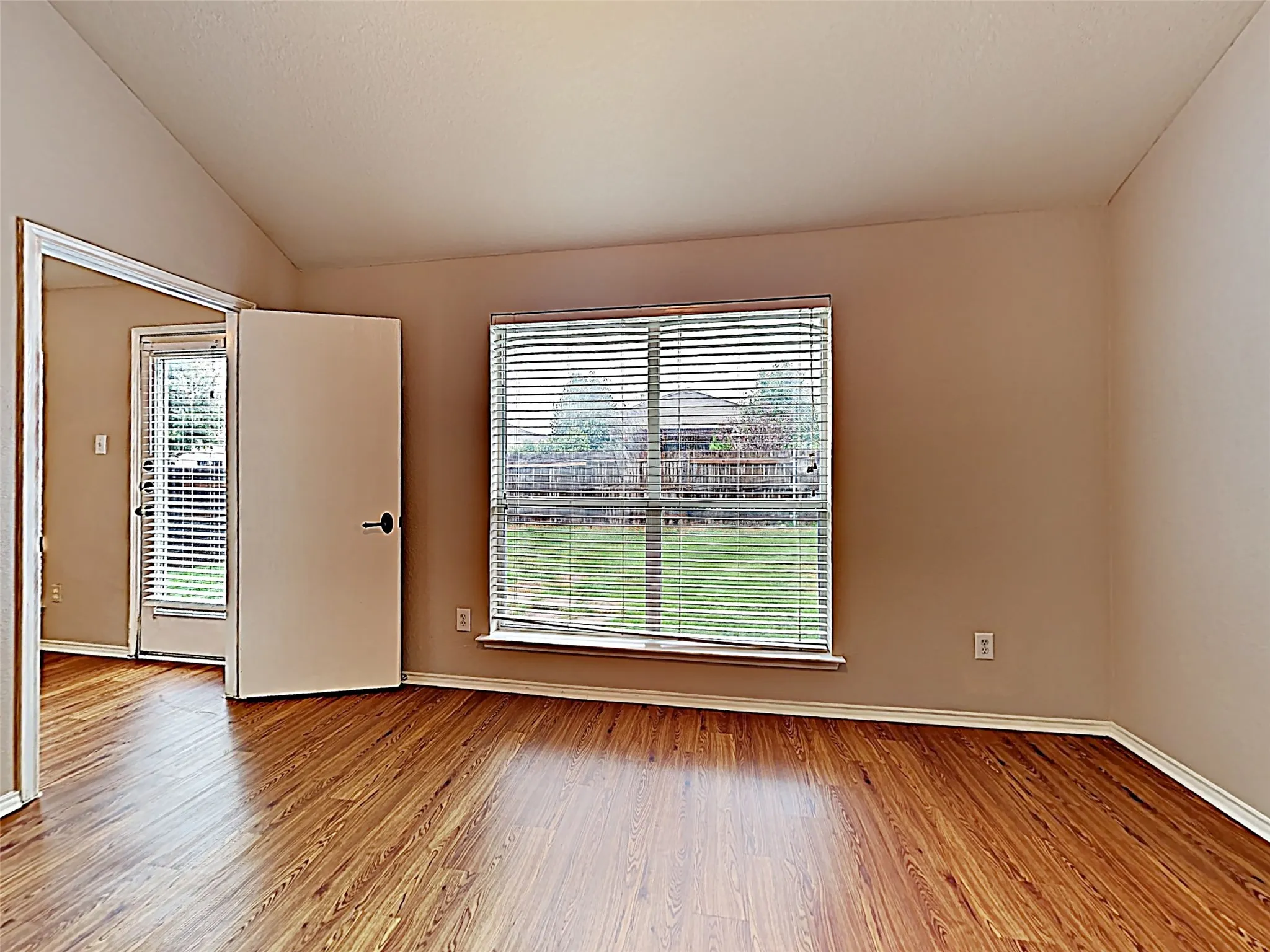 Spacious interior room featuring vaulted ceilings, wood-finish flooring, and a large window with horizontal blinds