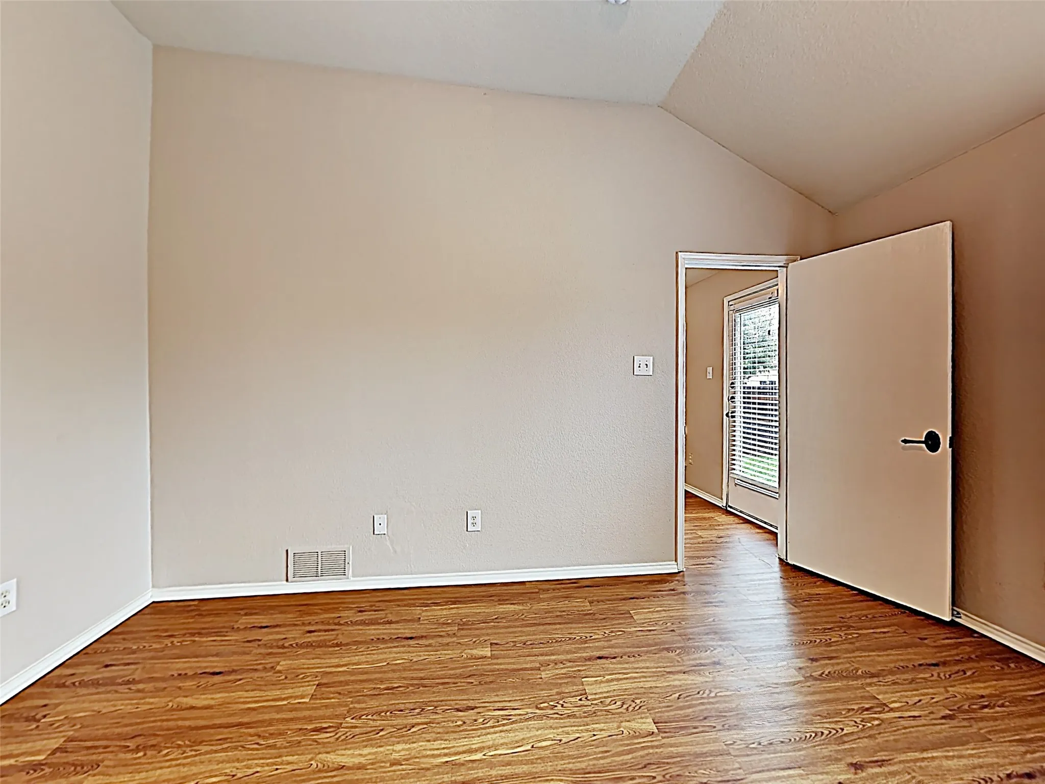 Room featuring vaulted ceilings, wood-finish flooring, light tan walls, white baseboards, and a doorway leading to an outdoor area with a glass panel door