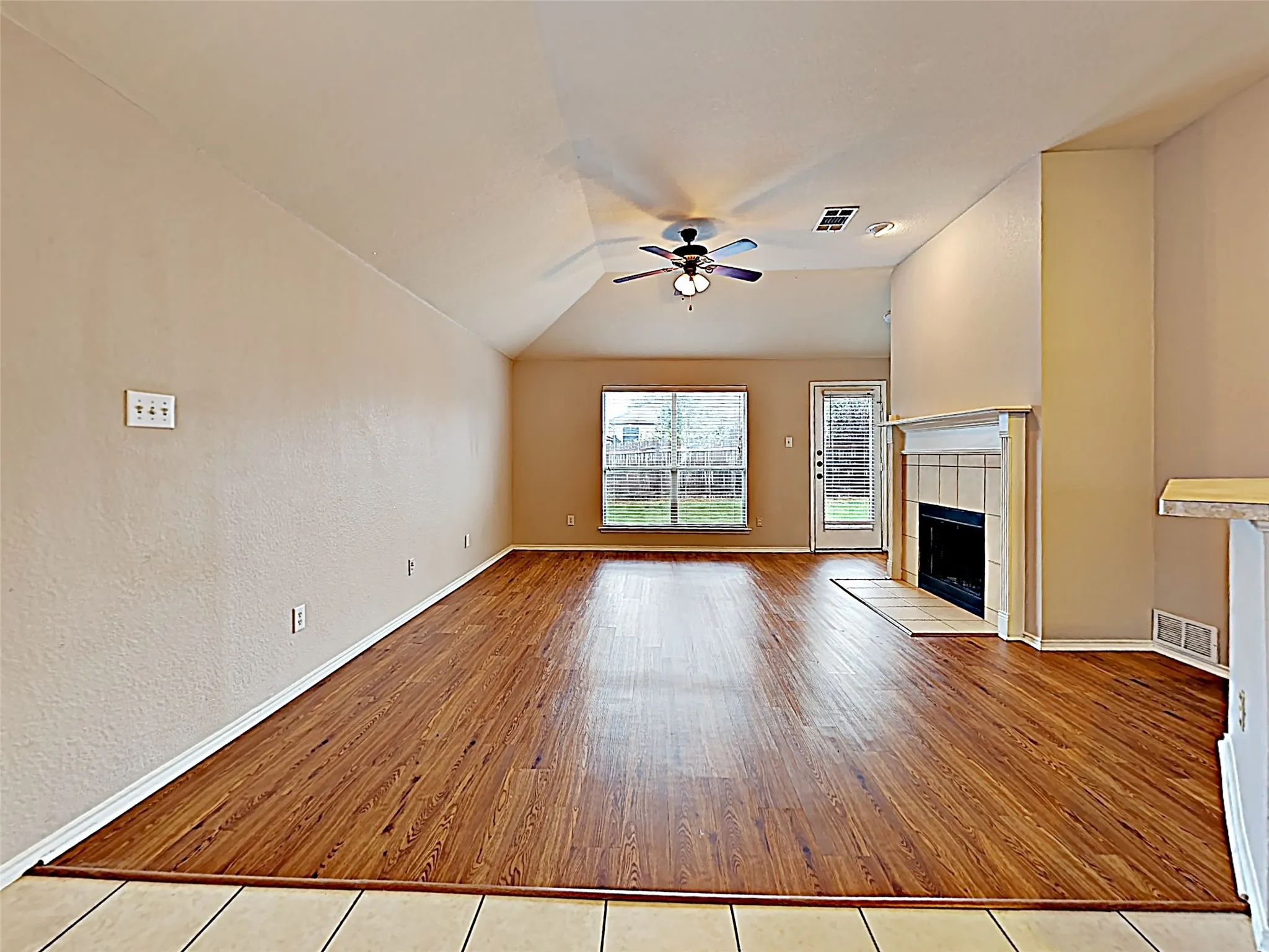 Open-concept living space featuring wood-finish flooring, a vaulted ceiling, and a ceiling fan with integrated lighting