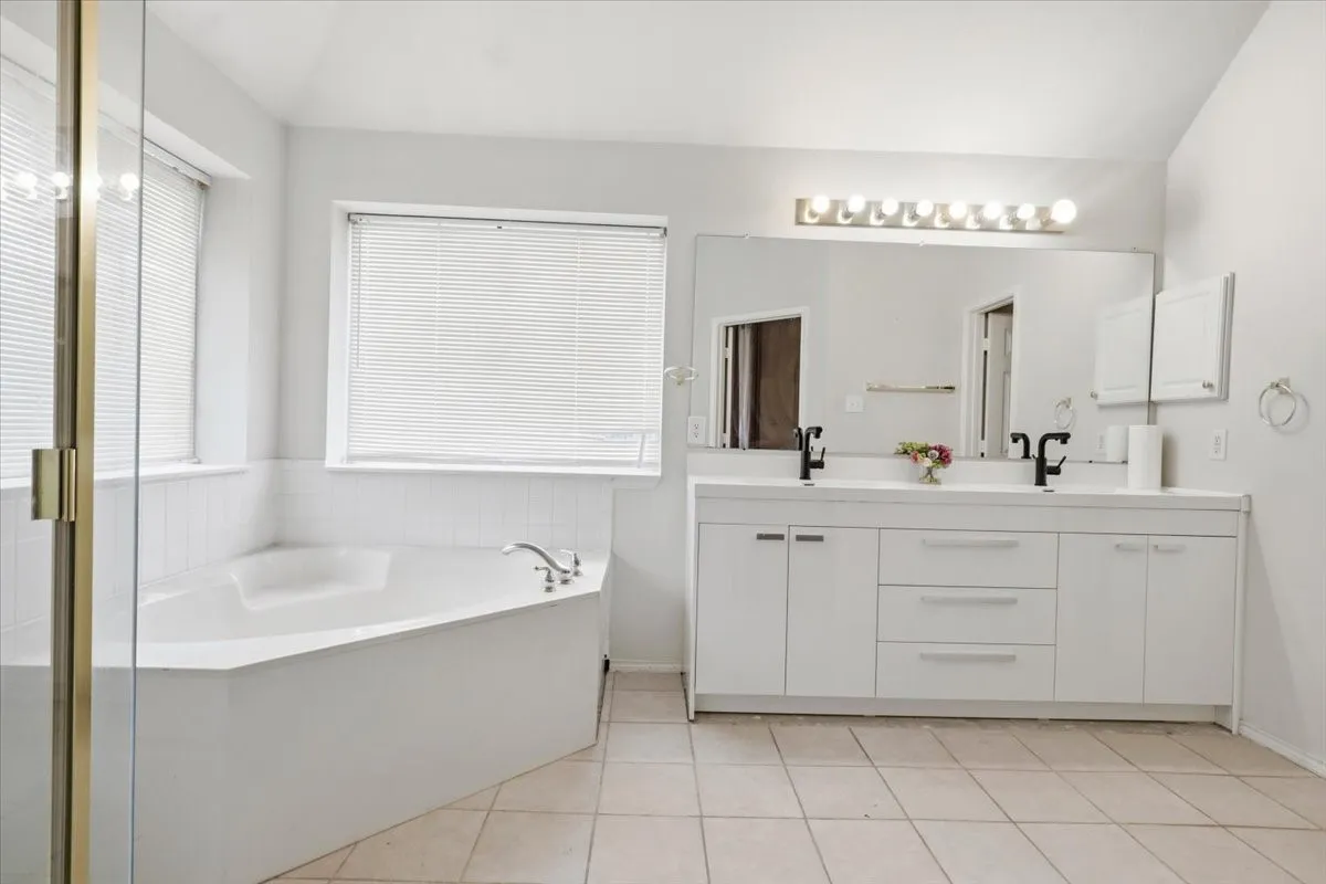 Spacious bathroom featuring a corner soaking tub, dual vanity with white cabinetry, matte black faucets, and a large wall-mounted mirror