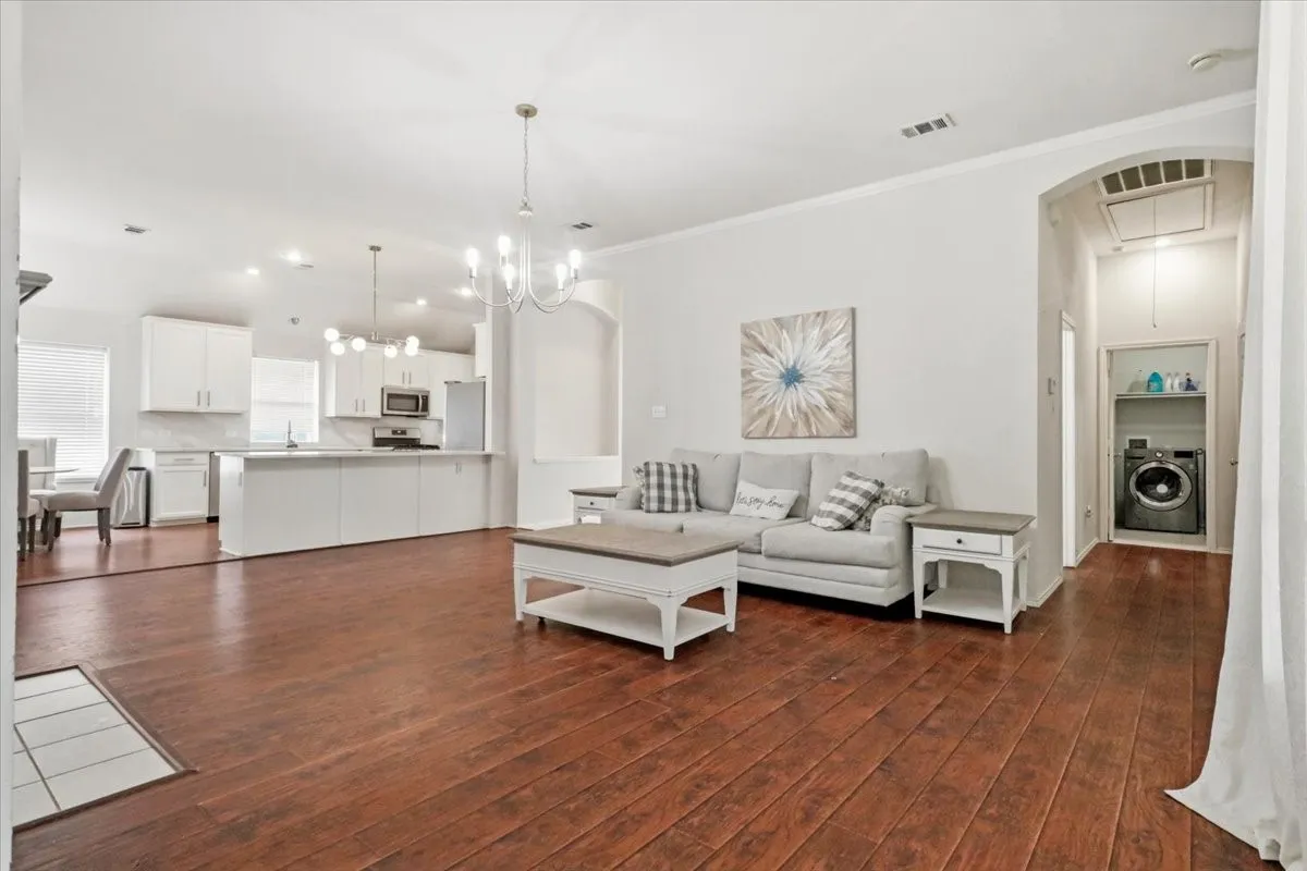 Spacious living area featuring rich wood-finish flooring and a contemporary chandelier