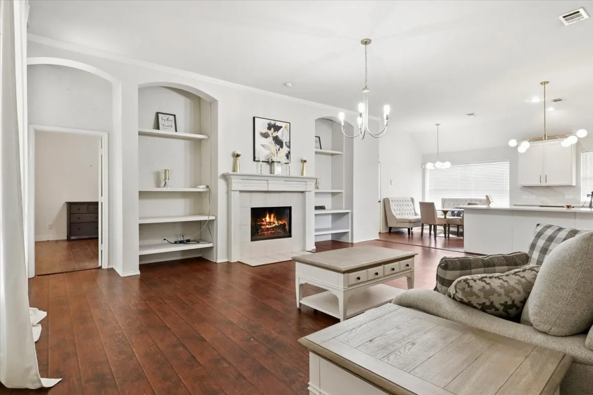 Spacious living area featuring wood-finish flooring, a tiled fireplace with a mantel, built-in shelving, and an arched entry