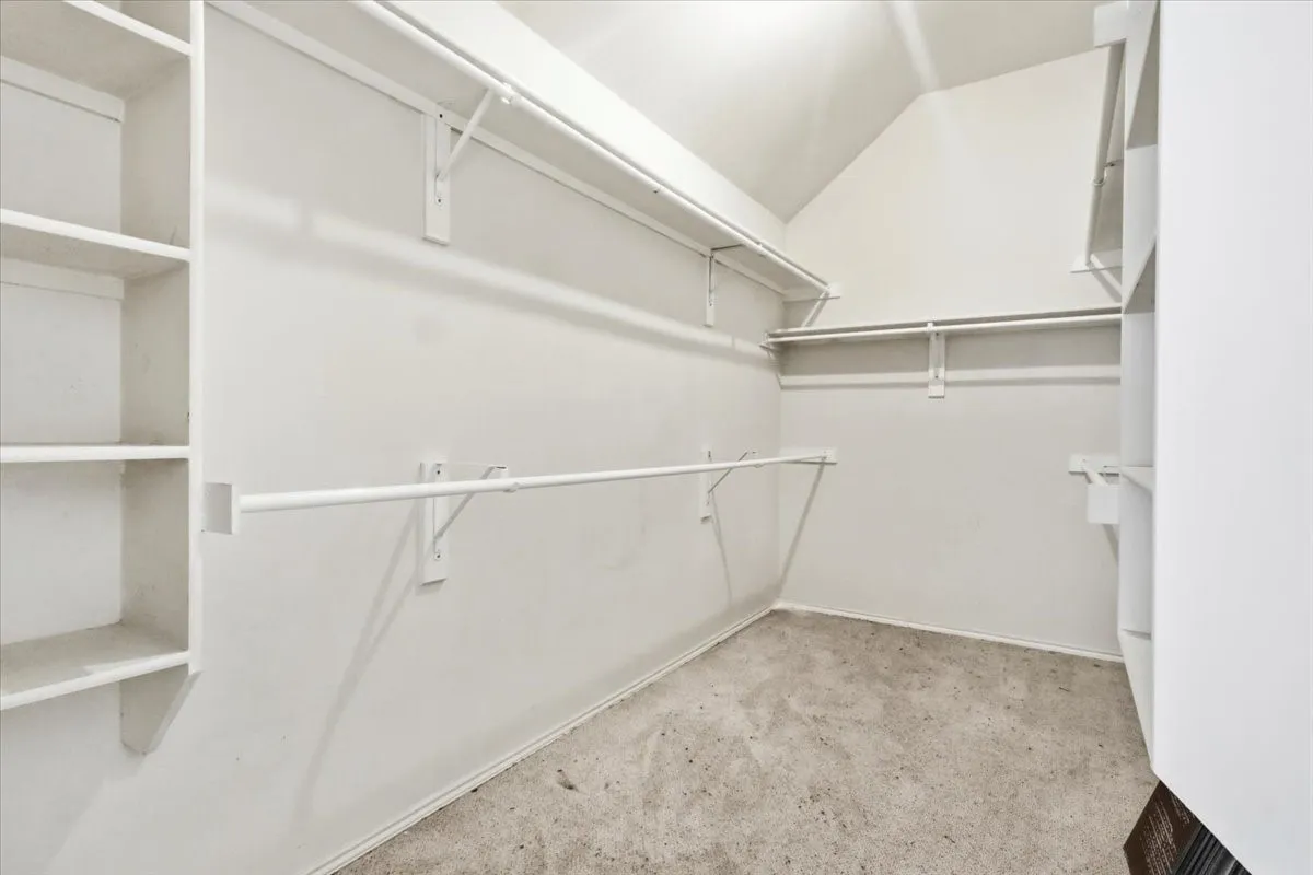 Walk-in closet with sloped ceiling, built-in shelving, multiple hanging rods, and carpet flooring