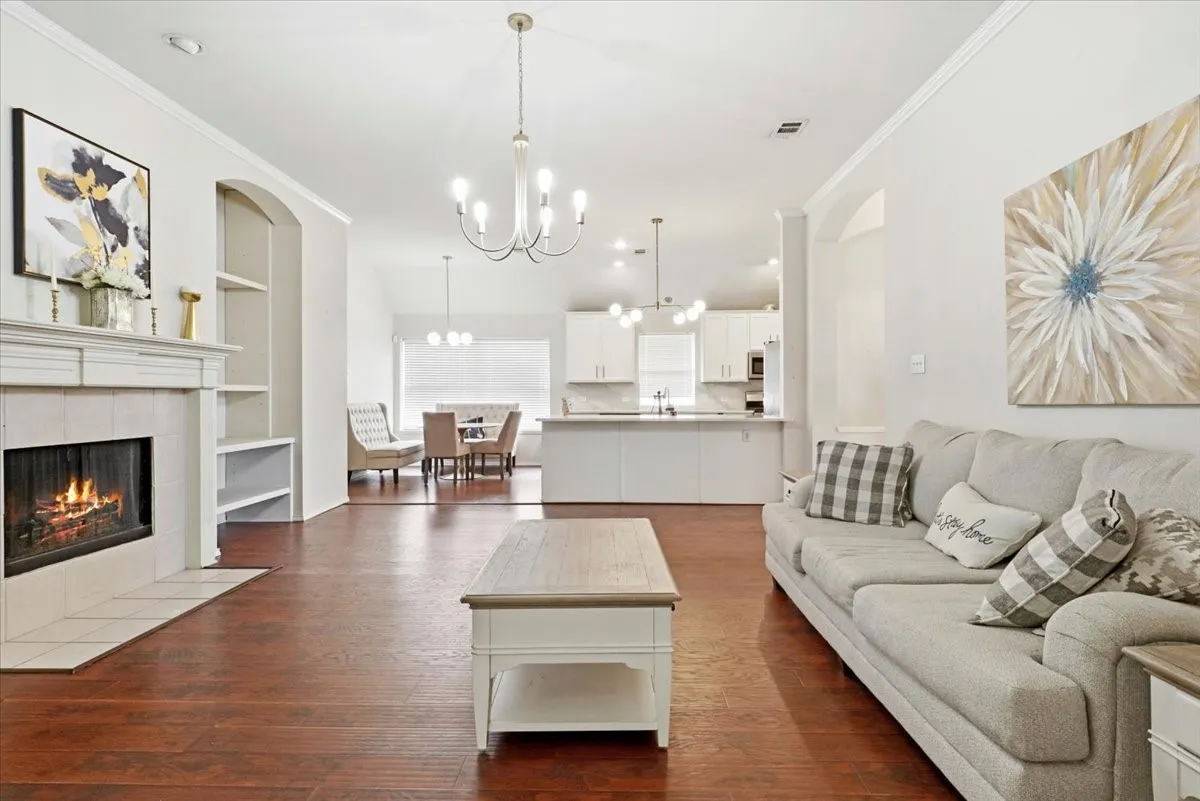 Living area featuring wood-finish flooring, a white mantel fireplace with tile surround, built-in shelving, and crown molding
