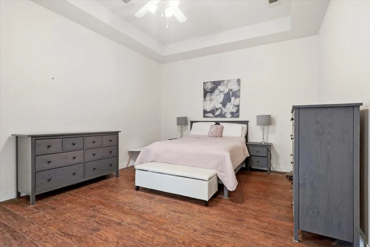 Spacious bedroom featuring wood-finish flooring, a tray ceiling, and a ceiling fan with integrated lighting