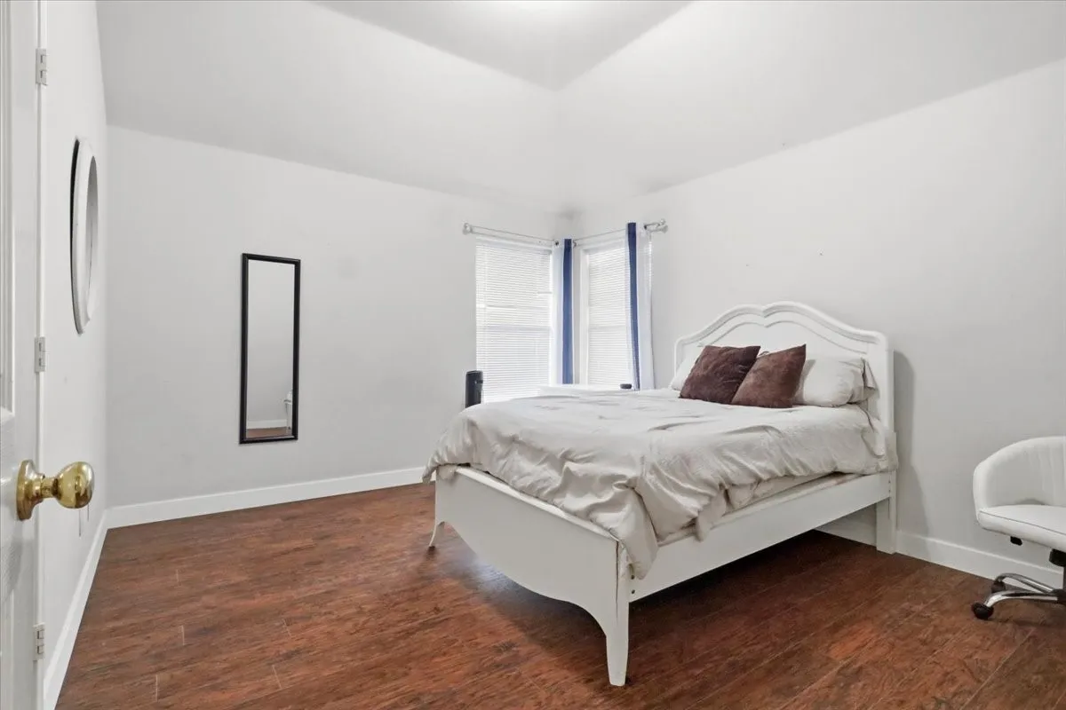 Bedroom featuring wood-finish flooring, white baseboards, and bright white walls
