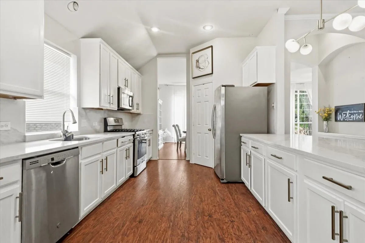 Bright kitchen featuring white cabinetry, stainless steel appliances, light countertops, wood-finish flooring, and recessed lighting