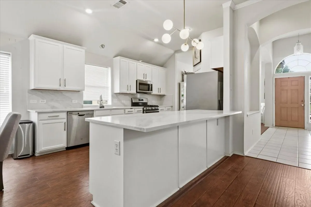 Contemporary kitchen featuring a large central island, white cabinetry, integrated stainless steel appliances, and wood-finish flooring