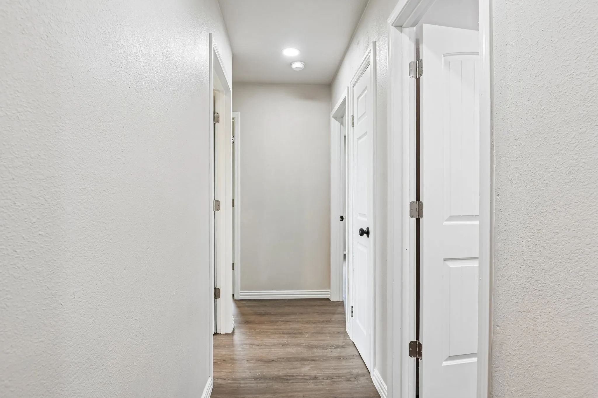 Hallway featuring wood-finish flooring, recessed lighting, and white paneled doors with dark hardware