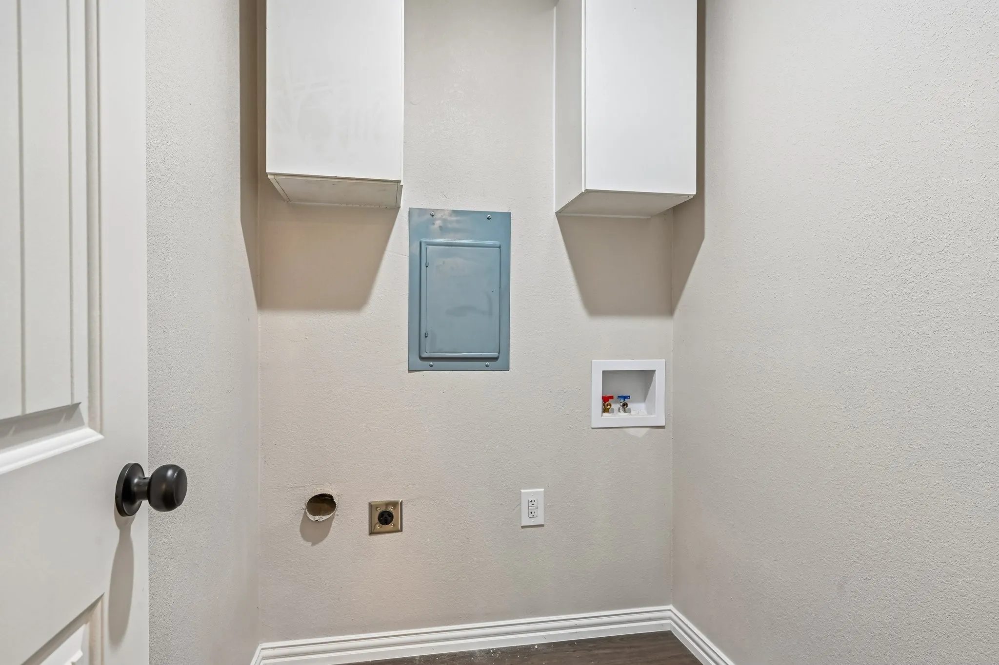 Dedicated laundry area featuring a white paneled door with a black knob, two white wall-mounted cabinets, and connections for laundry appliances