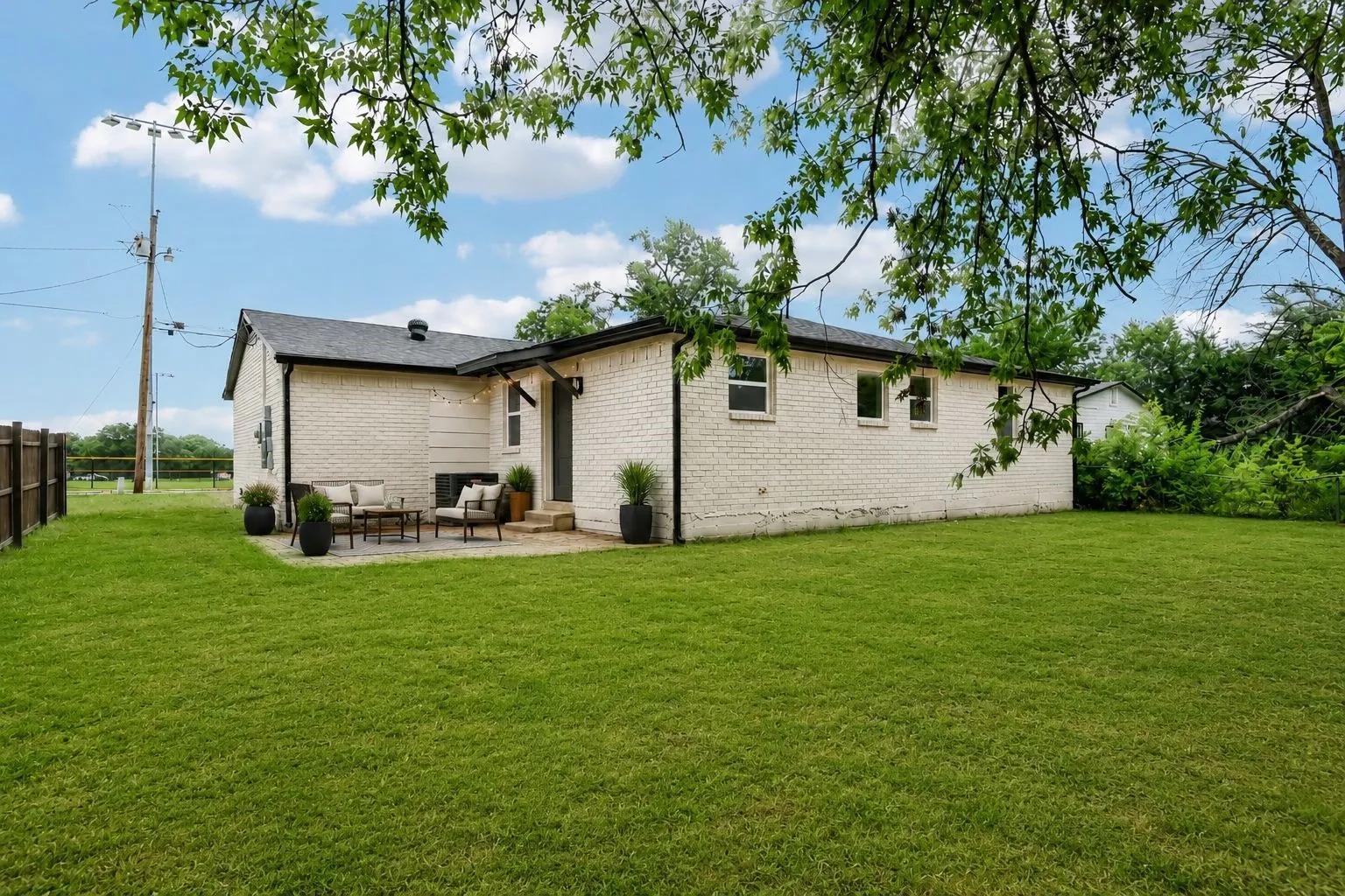 Expansive green lawn surrounds a white brick exterior with a black asphalt shingle roof