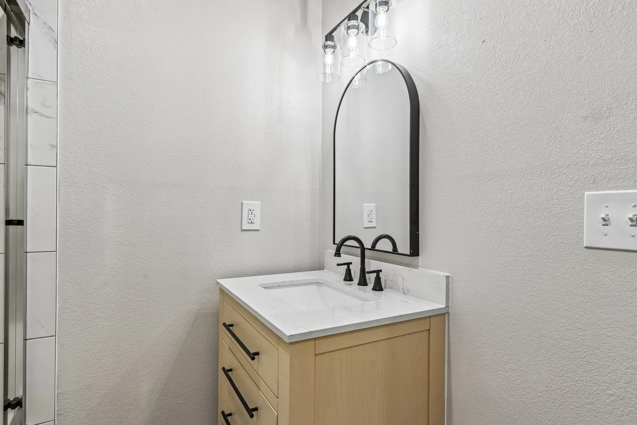 Modern vanity featuring light wood-finish cabinetry, a white countertop with integrated rectangular sink, and matte black hardware