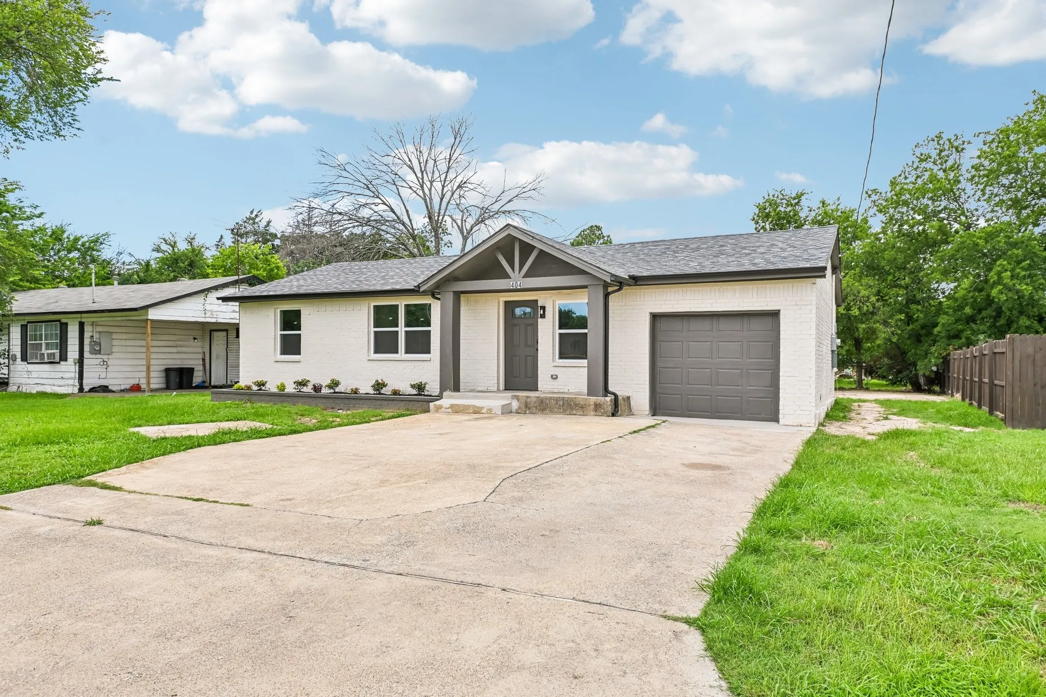White brick exterior featuring a dark gray garage door, a prominent front door with side window, a decorative gable over the entrance, and a concrete driveway