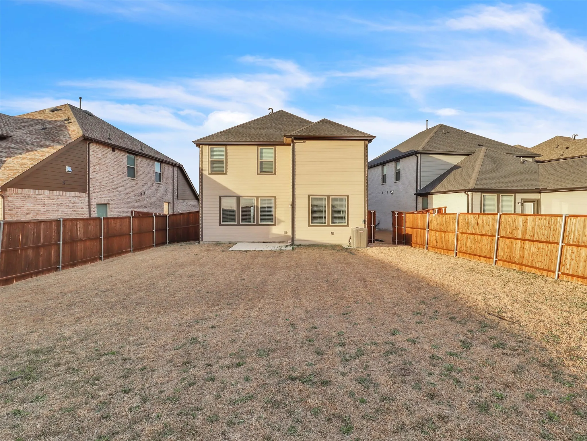 Rear exterior featuring a two-story design, multiple windows, a concrete patio, and a privacy fence