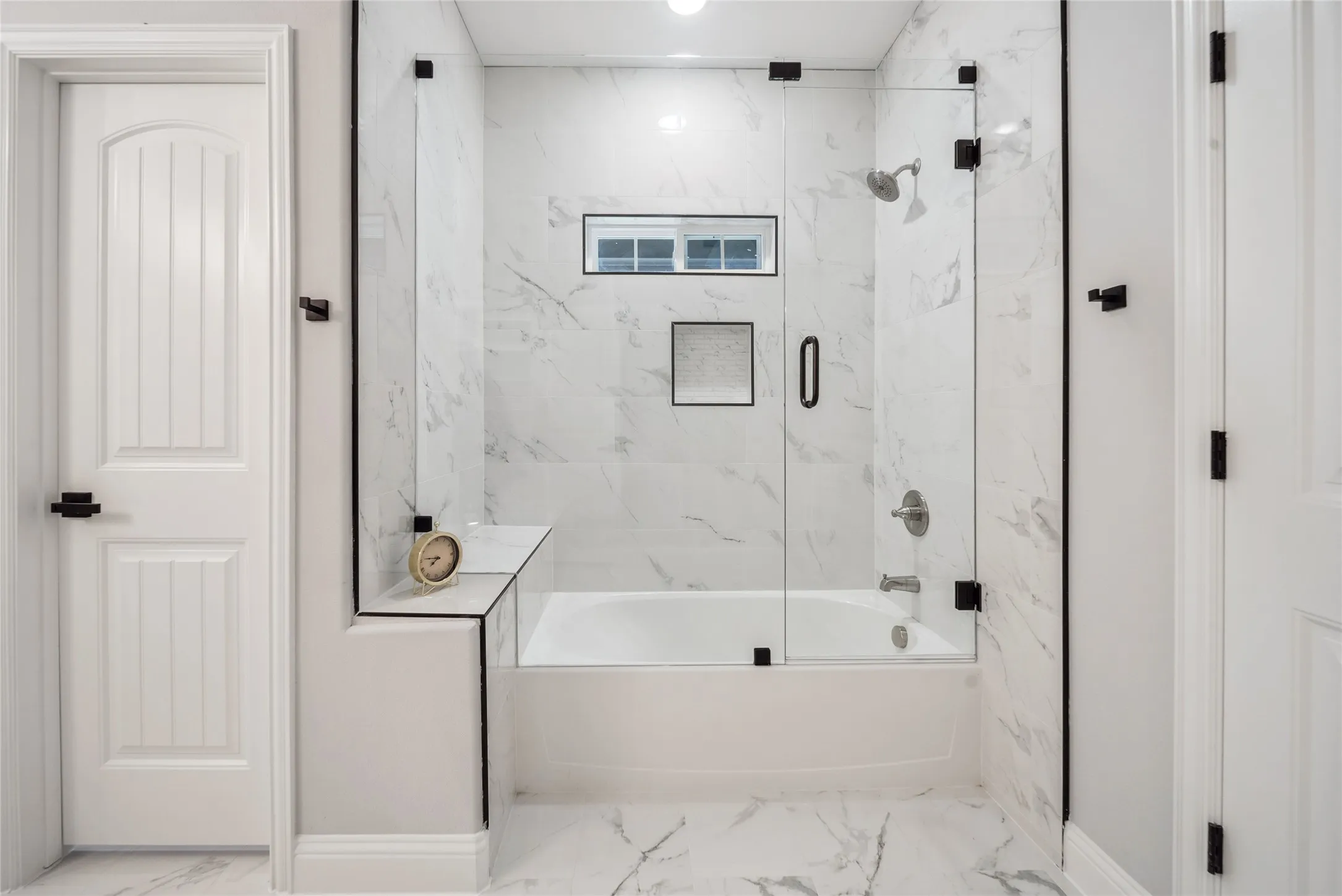 Bathroom featuring a bathtub with a clear glass enclosure and black hardware, white tile surround, and a recessed window
