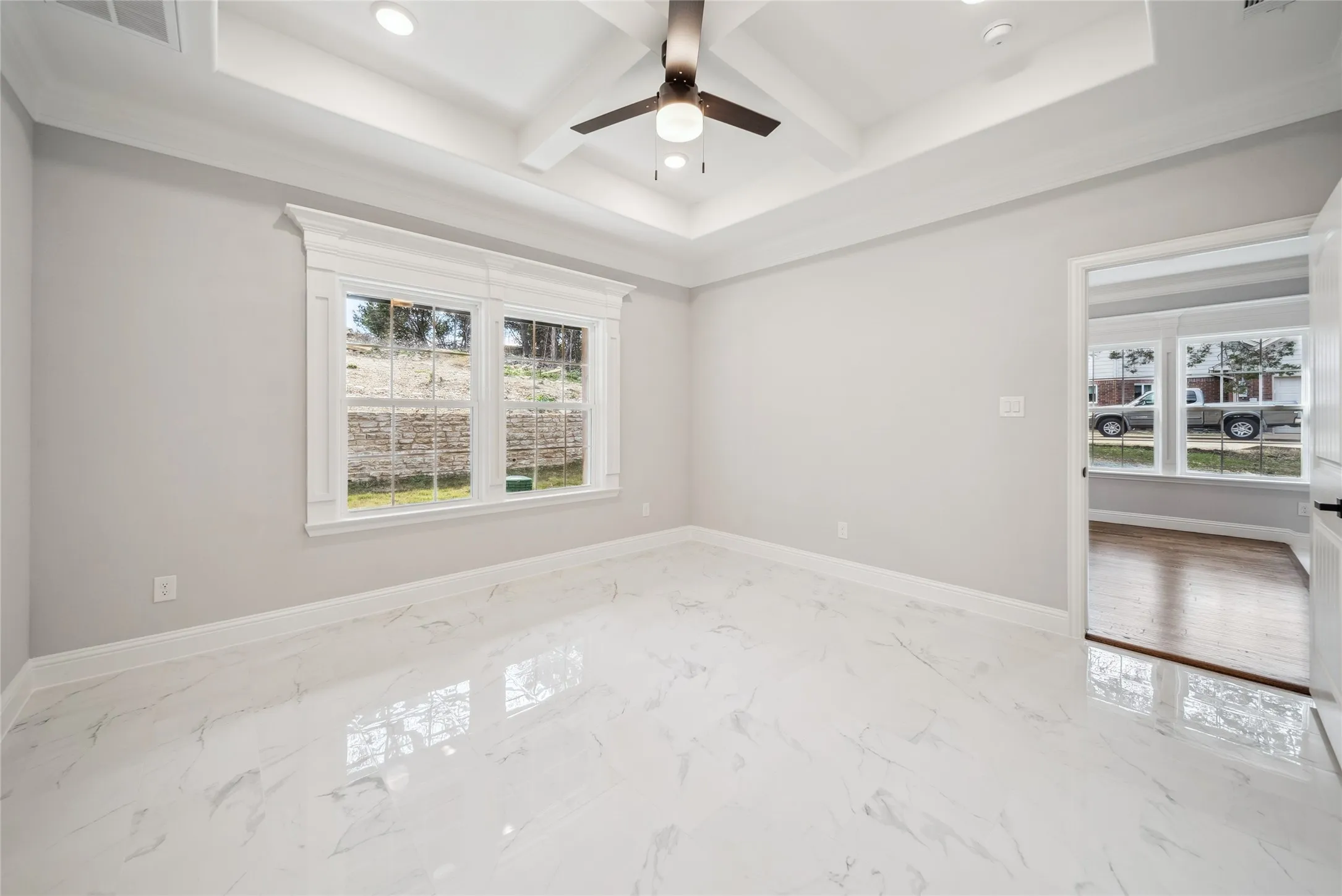 Spacious room featuring white marble-look flooring and a tray ceiling with recessed lighting