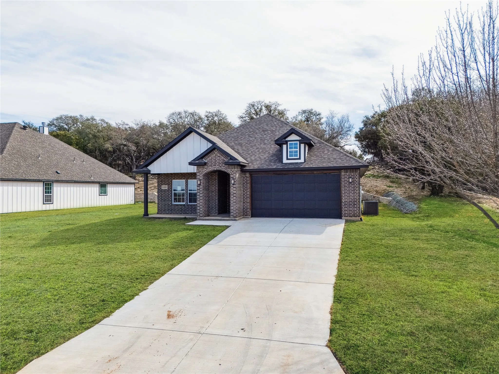Single-story home featuring a brick facade with white vertical siding accents, a dark shingle roof, and a prominent front entry with an arched portico