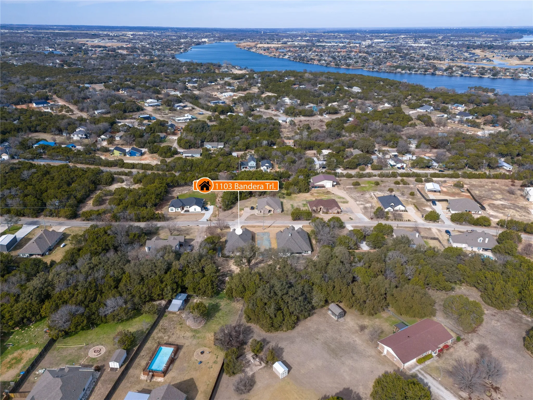 Aerial perspective showcasing a residential property within a treed neighborhood, featuring nearby water body