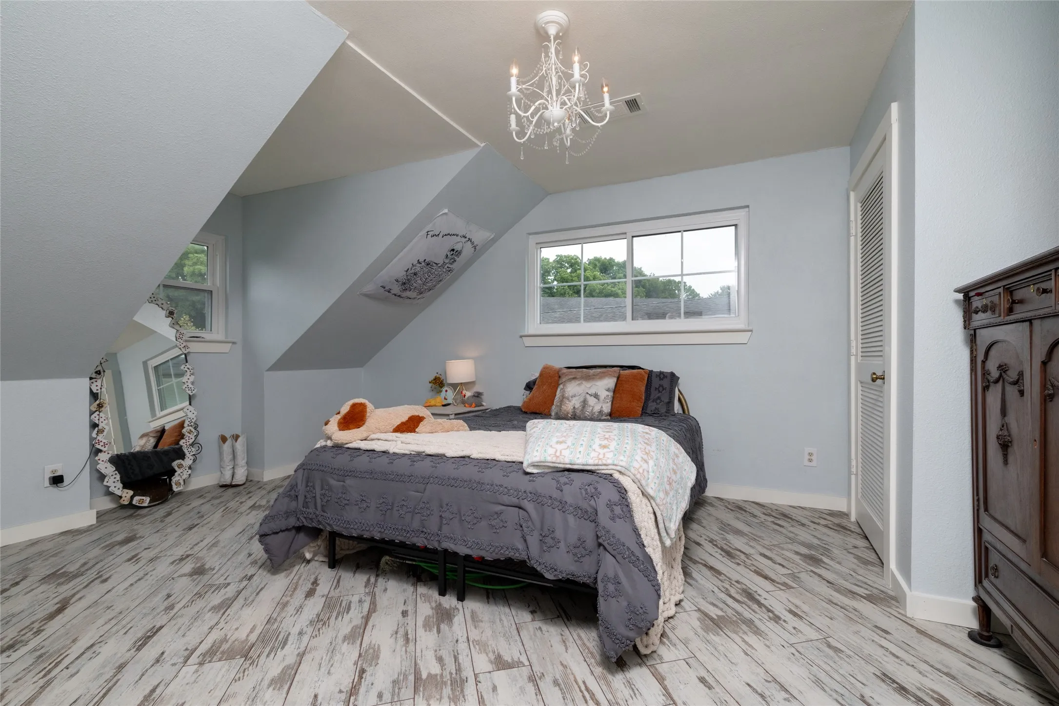 Attic bedroom featuring pitched ceilings, wood-finish flooring, multiple windows, a louvered bi-fold door, and a decorative chandelier