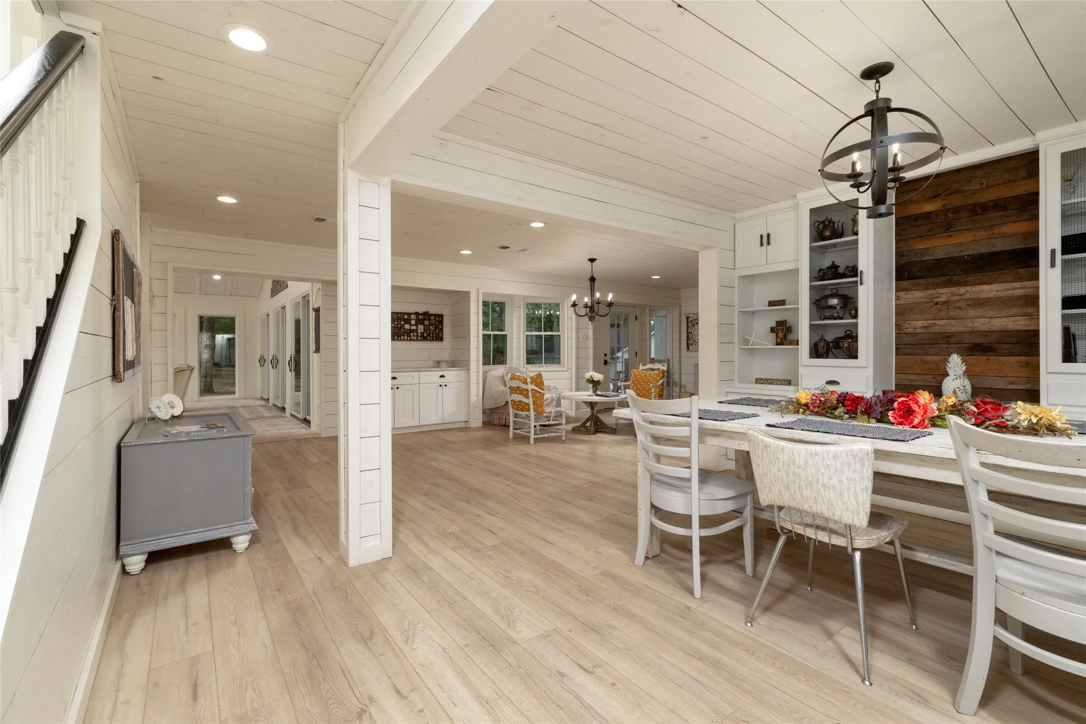 Spacious interior featuring light wood-finish flooring, white shiplap walls and ceiling, recessed lighting, and a white staircase with a dark wood handrail