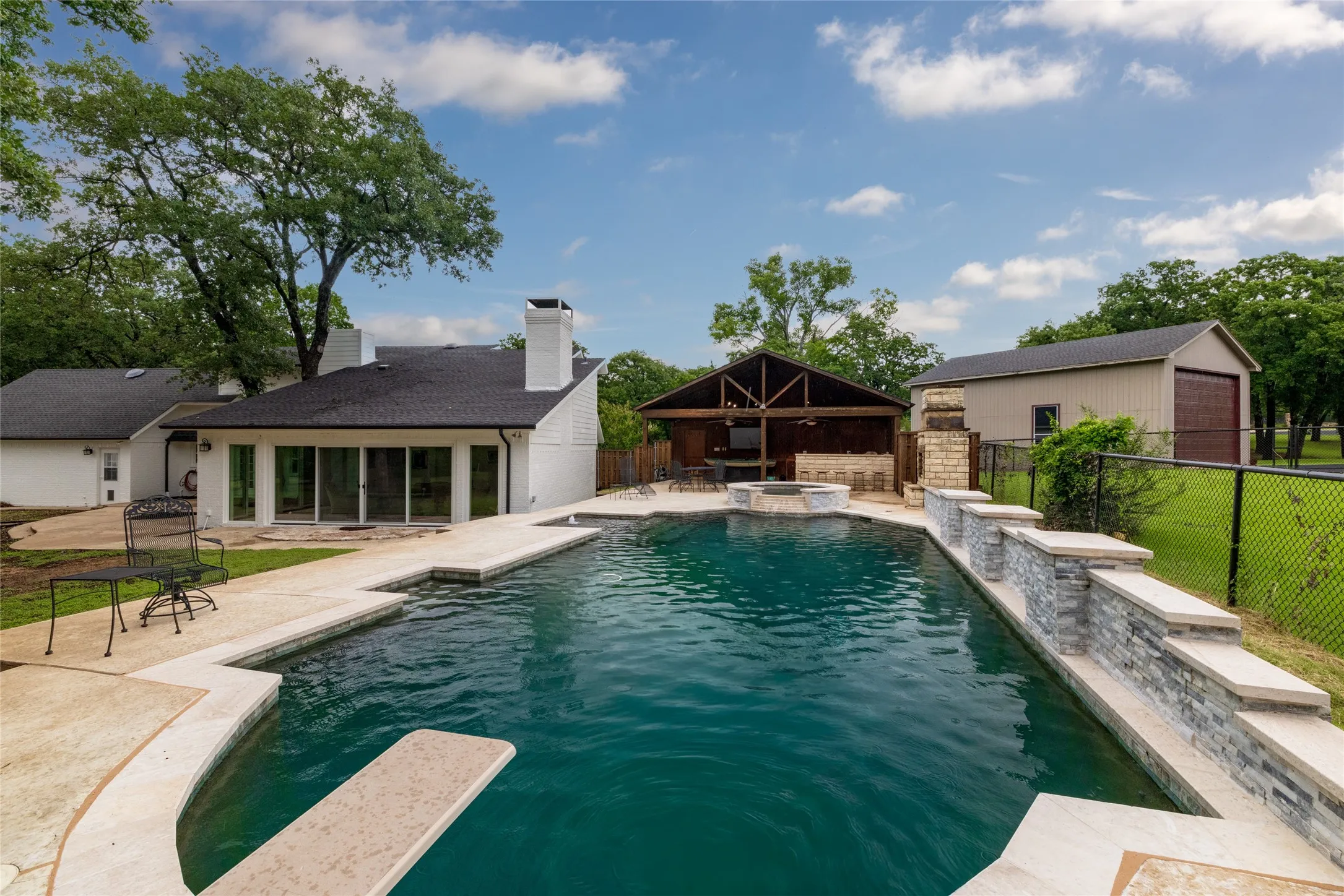 Expansive backyard featuring a large swimming pool with diving board, surrounded by light-colored concrete decking